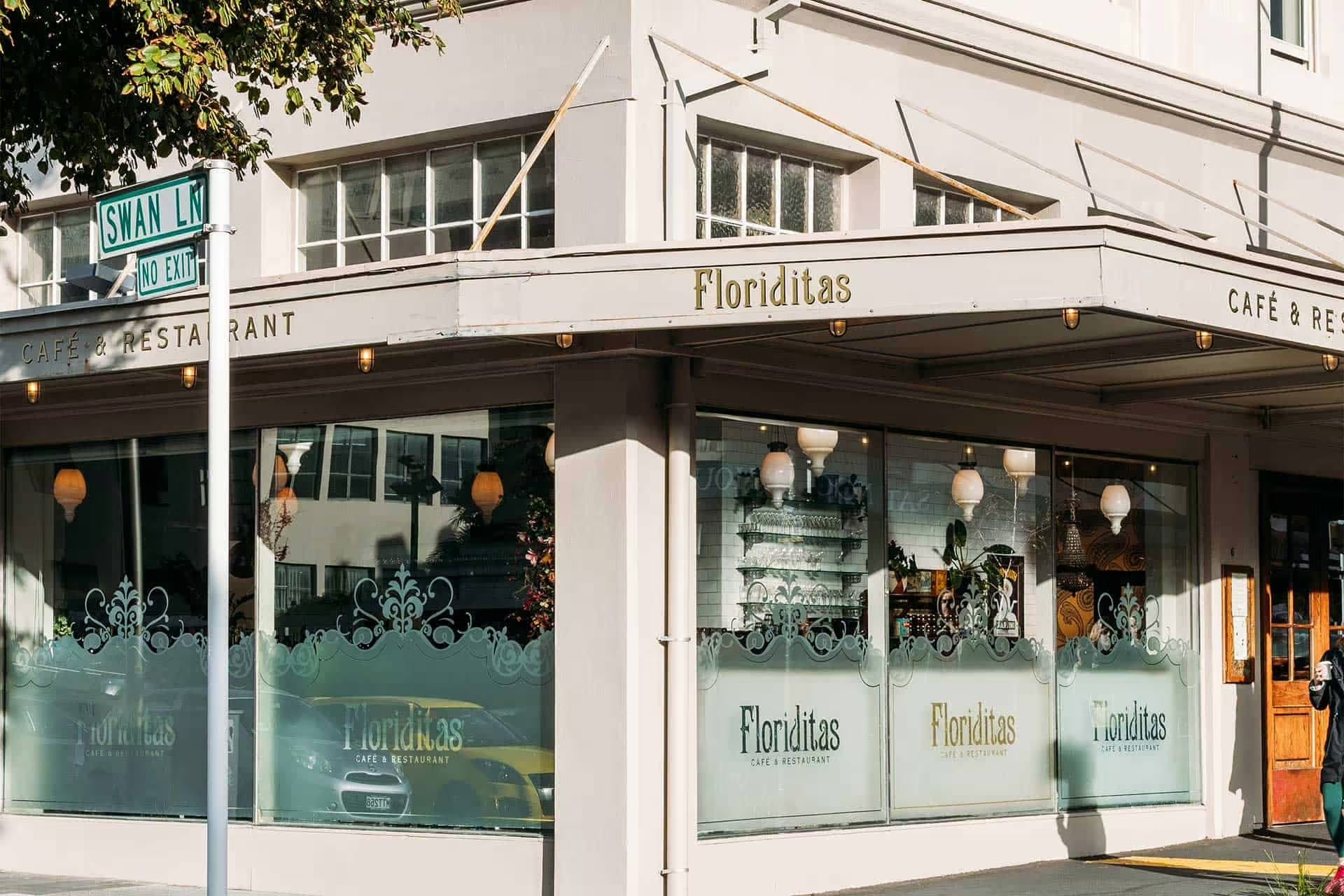 Street corner view of Floriditas café and restaurant with large windows and a Swan Ln street sign.