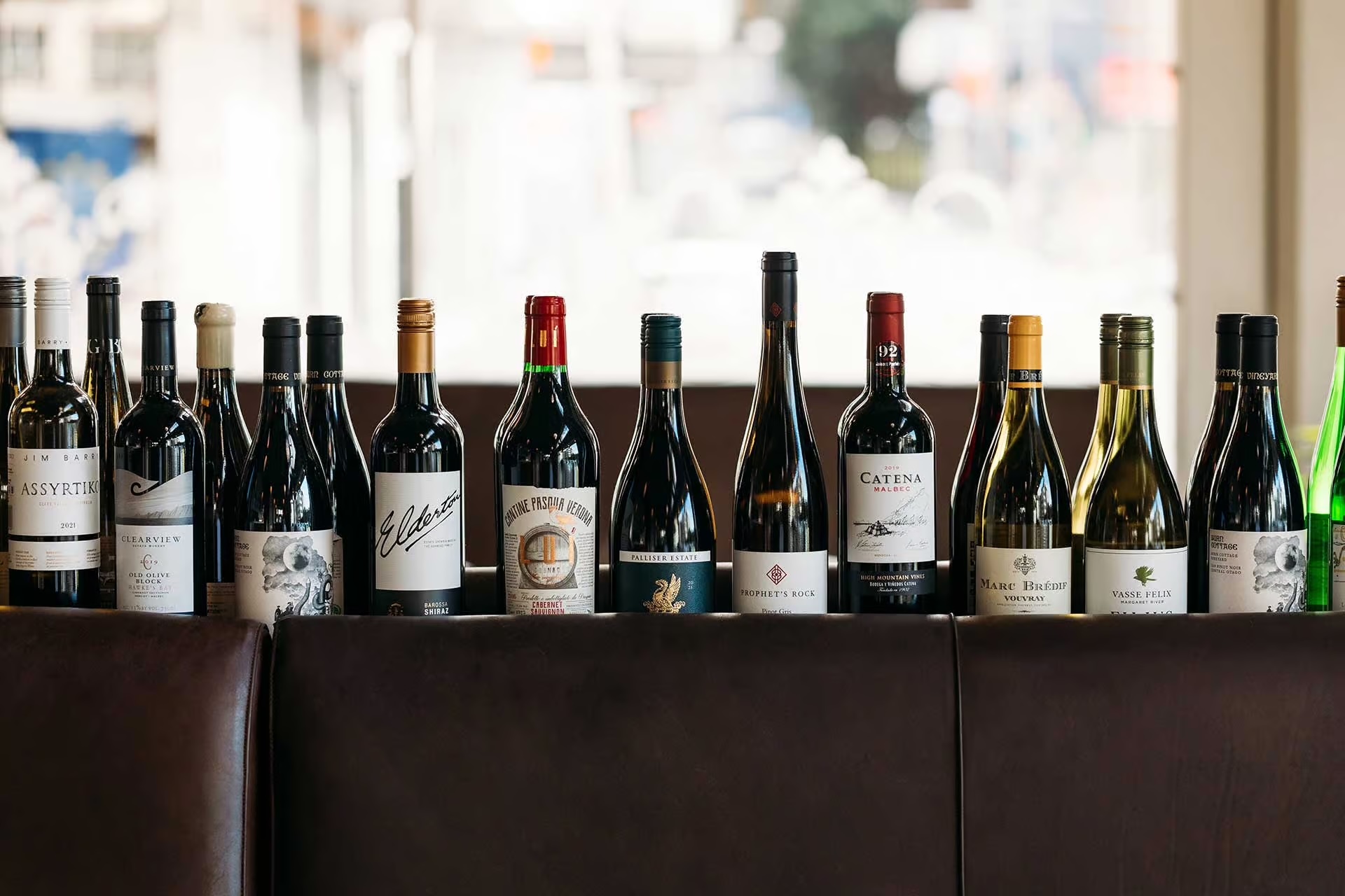 Row of various wine bottles displayed on a dark surface with a blurred background.