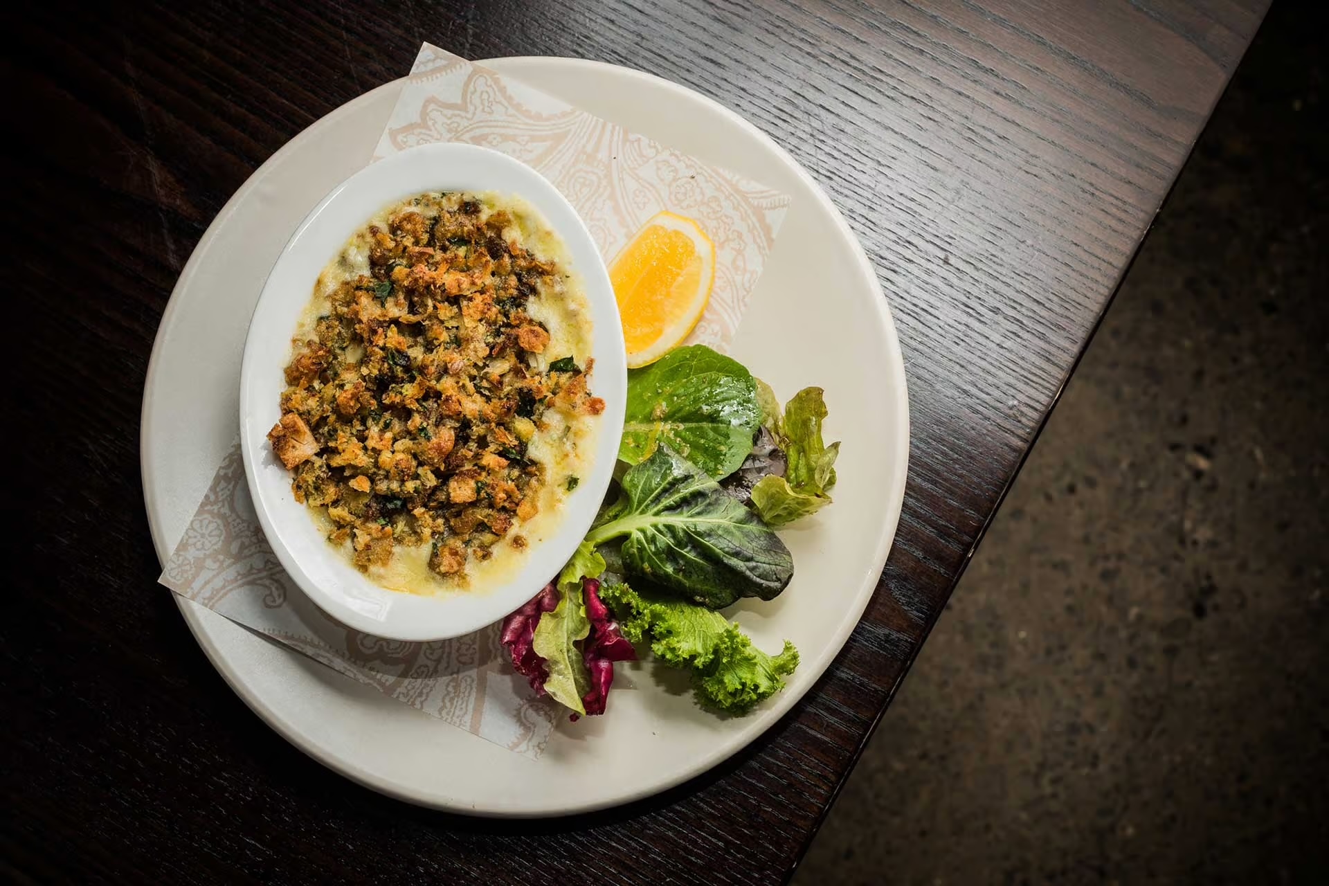 Baked dish with crispy breadcrumb topping served with mixed greens and a lemon wedge on a white plate.