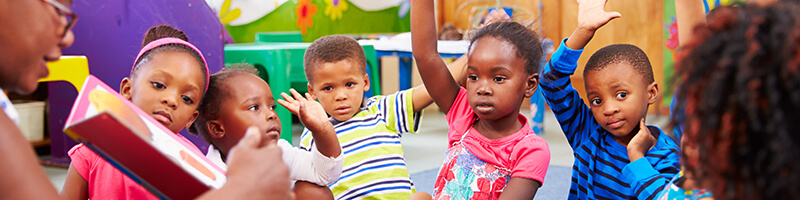 Group of 6 Black kids in a story time circle. Some have their hands raised. This is meant to represent the potential audience of educators and some silent auction ideas to target them.