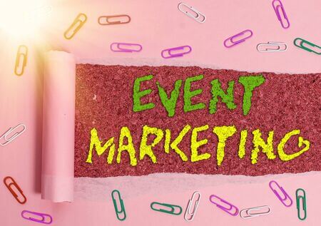 The words “Event Marketing” are shown in green and yellow text, respectively, against a dark pink background. In the foreground are various colors of paperclips and a torn pink paper. 