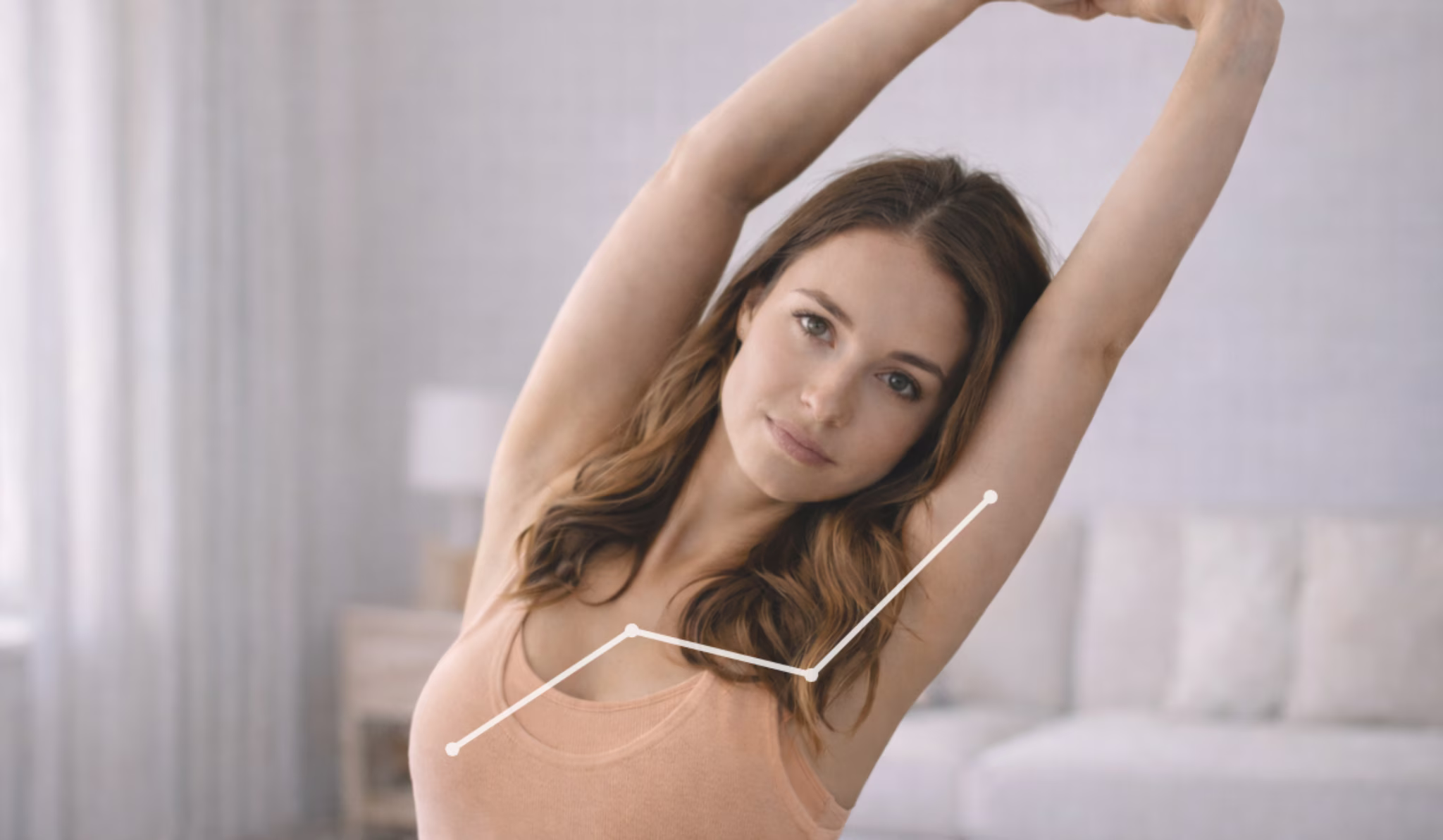 Woman in pink tank top stretching arms above her head in a softly lit living room.