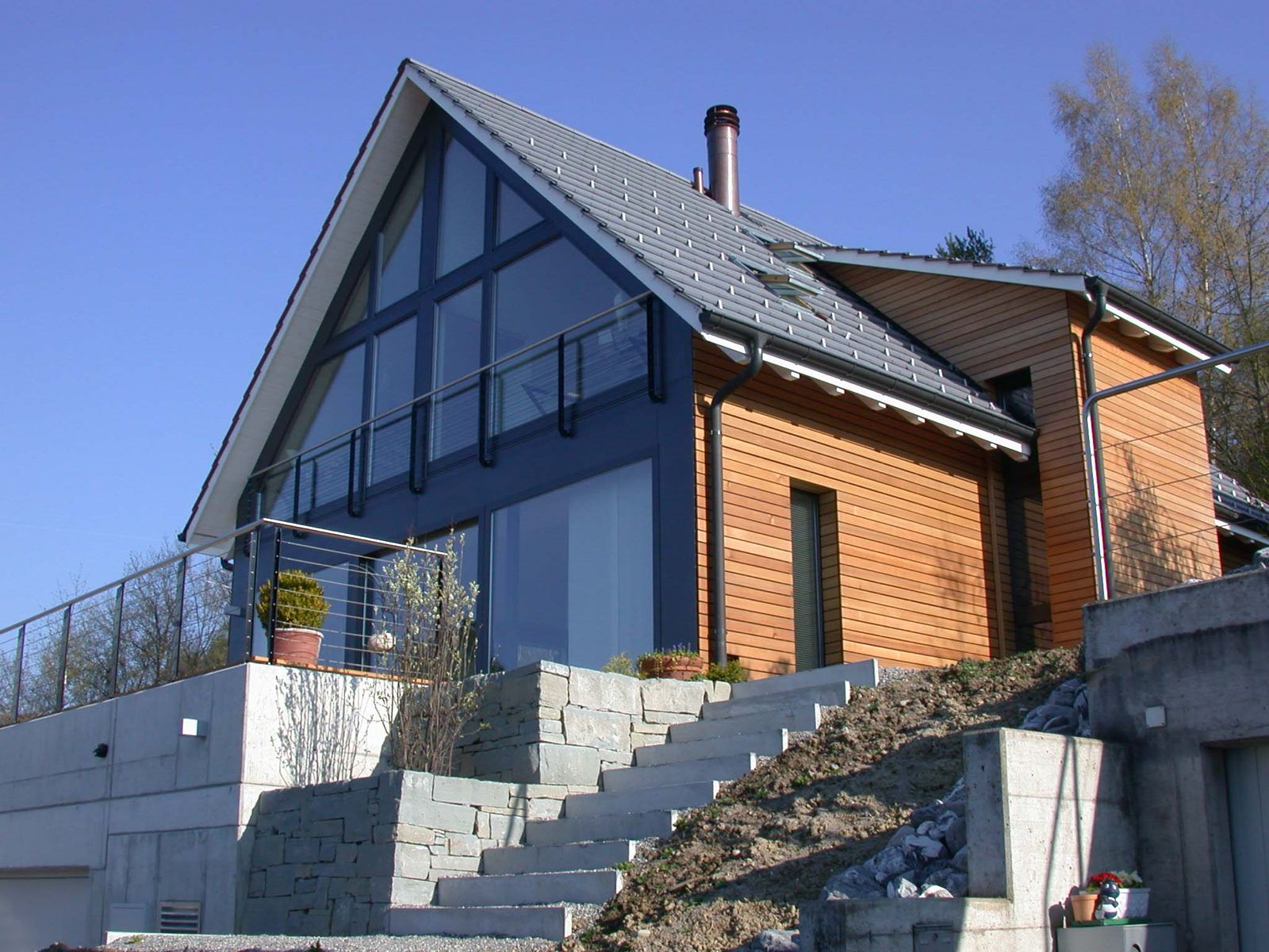 Modernes Haus mit großer Glasfassade, Holzverkleidung und Treppe aus Betonstufen an sonnigem Tag.
