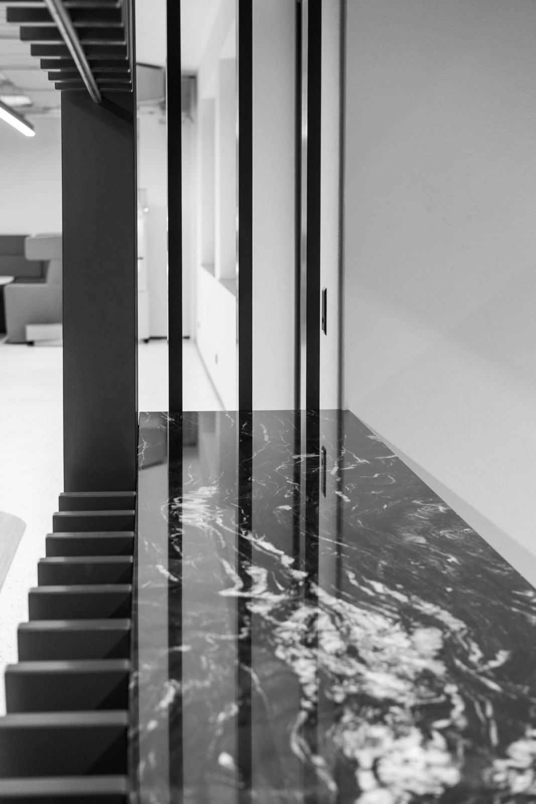 Schwarz-weißer Blick auf eine glänzende, marmorierte Oberfläche neben vertikalen, schwarzen Metallstäben in einem modernen Innenraum.