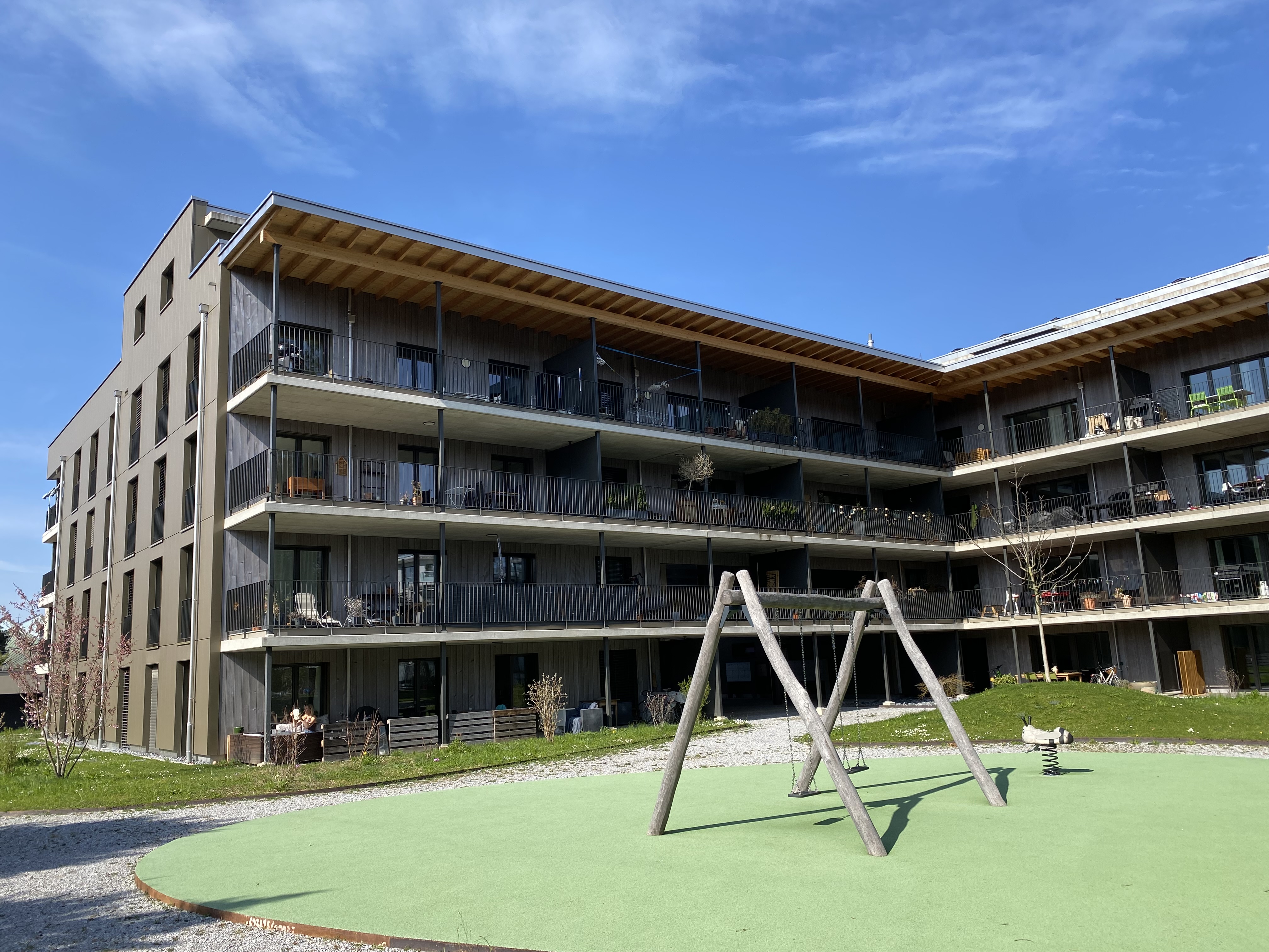 Modernes zweistöckiges Haus mit weißen Wänden, großen Fenstern und eingezäuntem Garten vor bewaldetem Hügel.