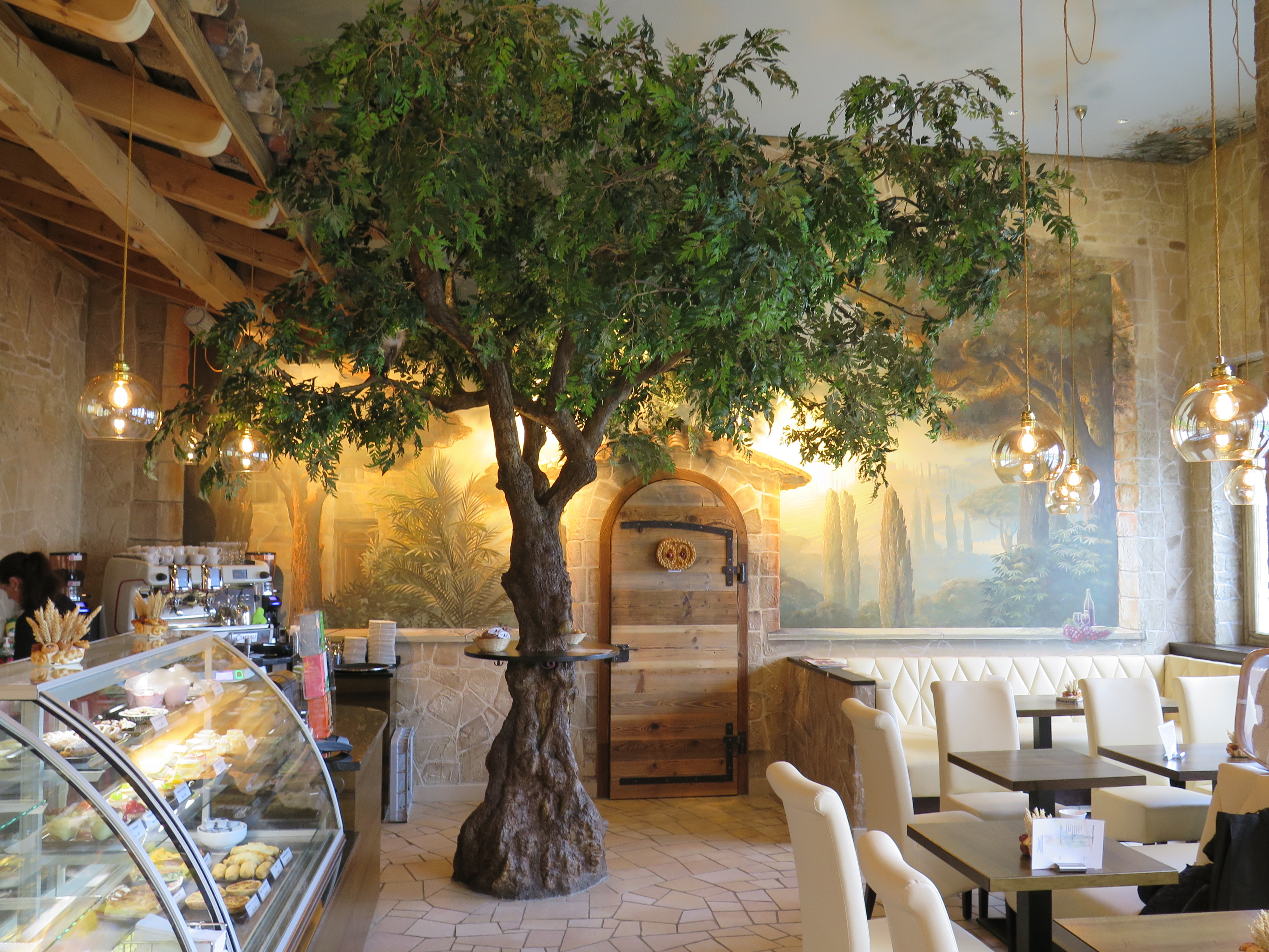 Modernes zweistöckiges Haus mit weißen Wänden, großen Fenstern und eingezäuntem Garten vor bewaldetem Hügel.