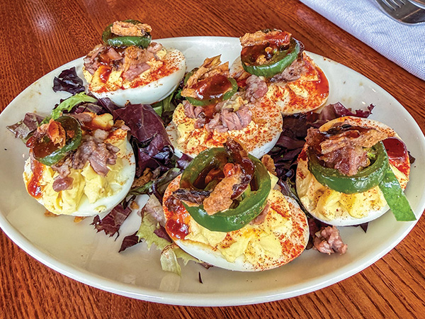 a plate of deviled eggs topped with brisket and candied jalapeño