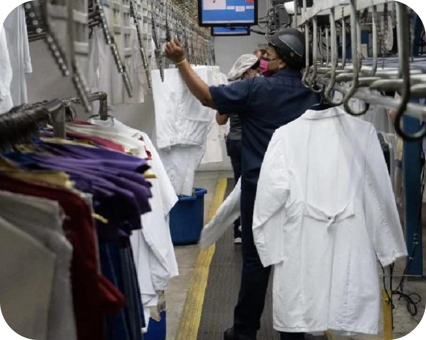 Workers handling white lab coats on a conveyor system in a laundry or garment processing facility.