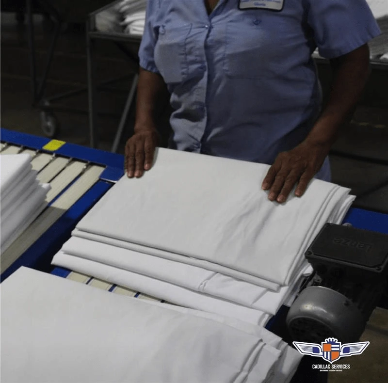 Person folding white linens on a conveyor belt in a laundry facility.