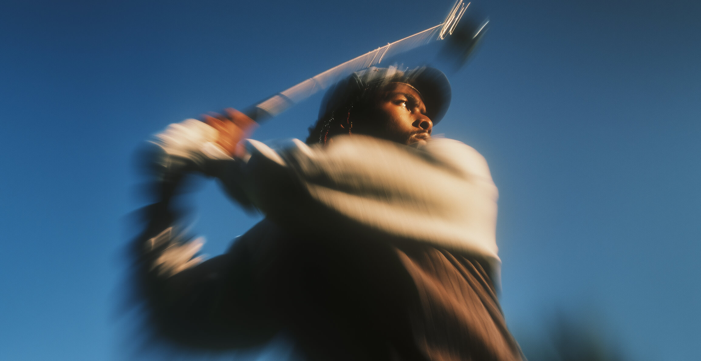 Man playing golf, captured mid-swing with motion blur against a clear blue sky.