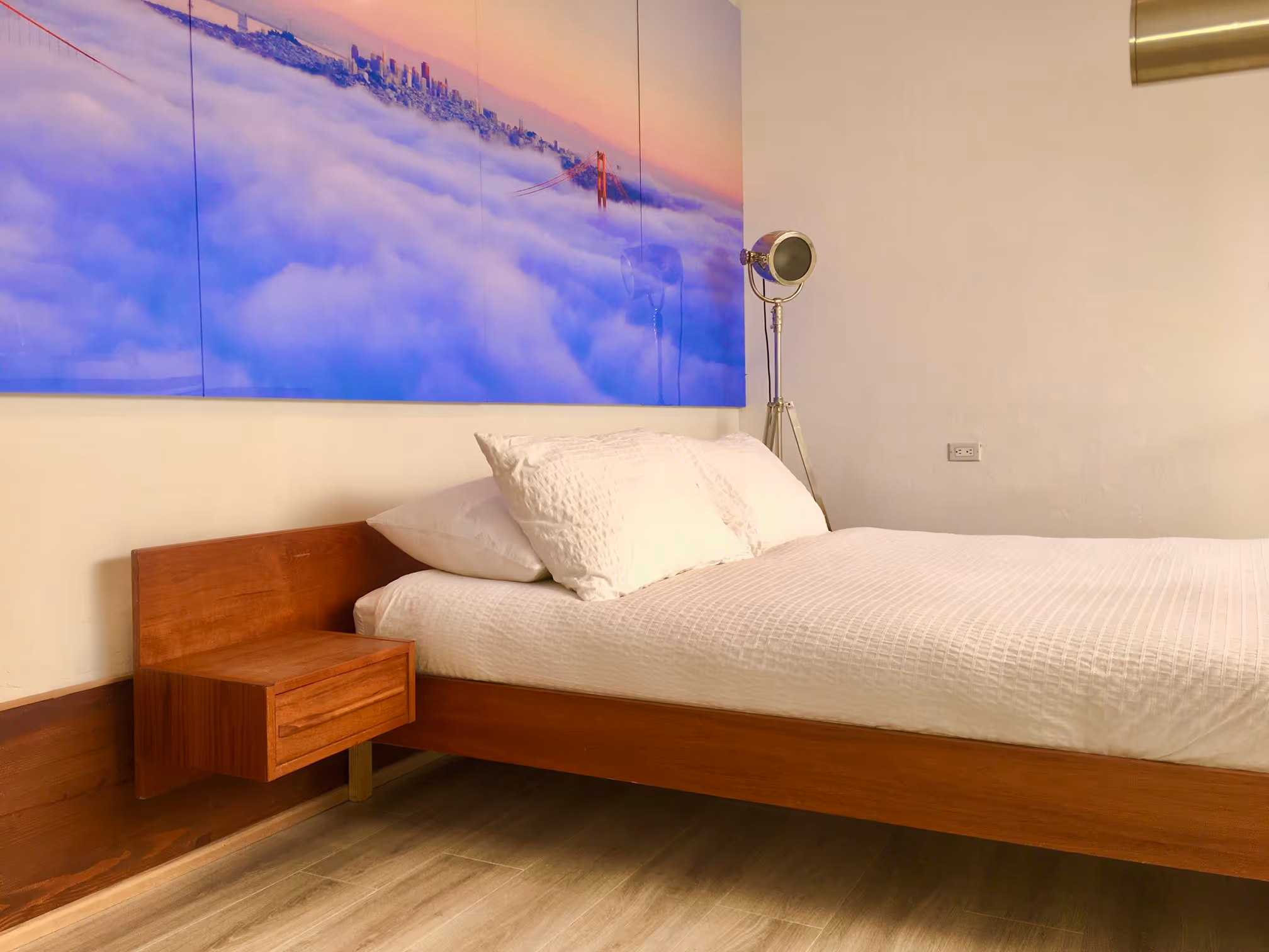 Minimalist bedroom with a wooden bed frame, white bedding, a floating wooden nightstand, and a large wall art.