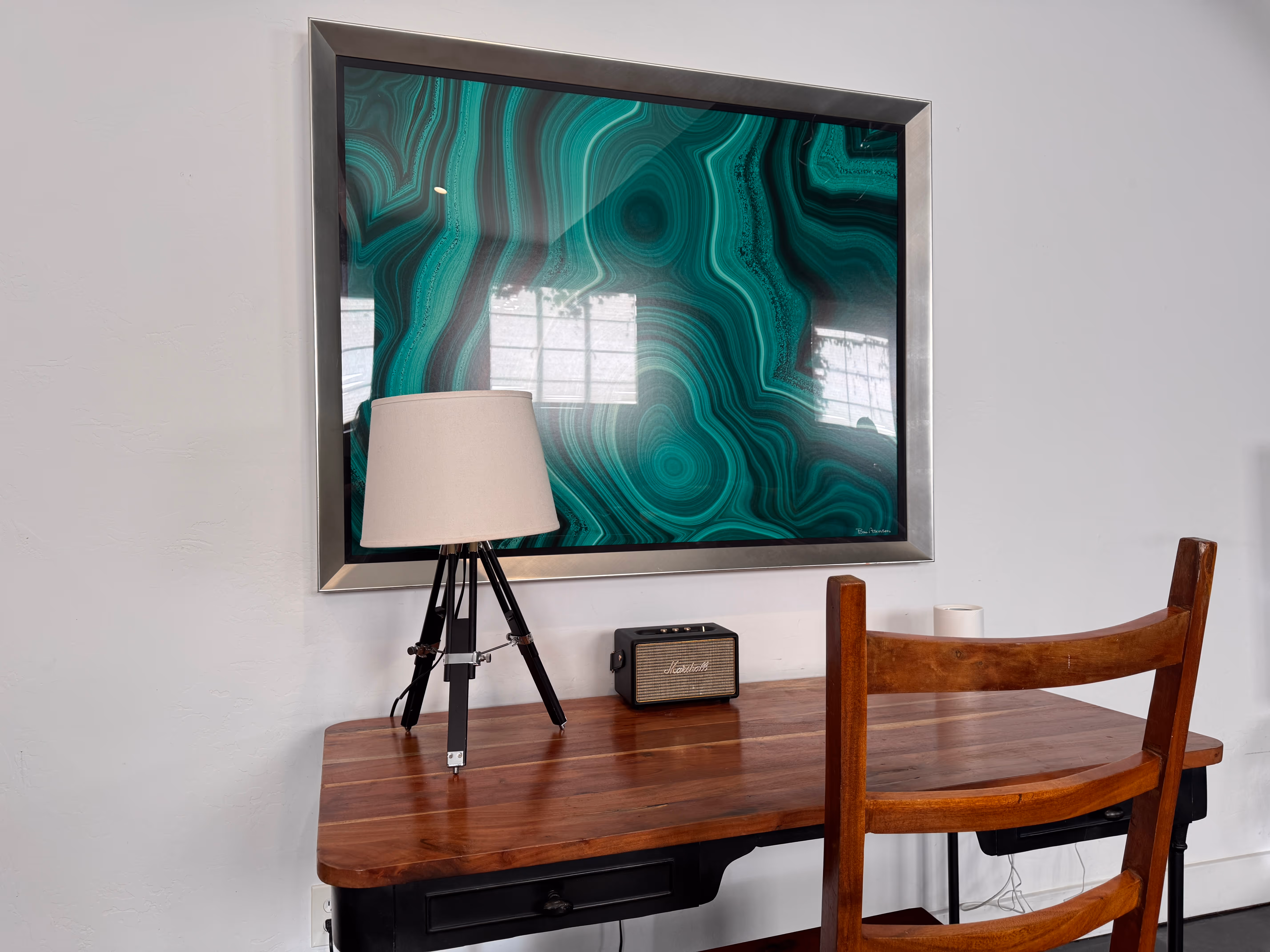 Wooden desk with a tripod lamp, a vintage Marshall speaker, and a wooden chair under a framed green abstract wall art.