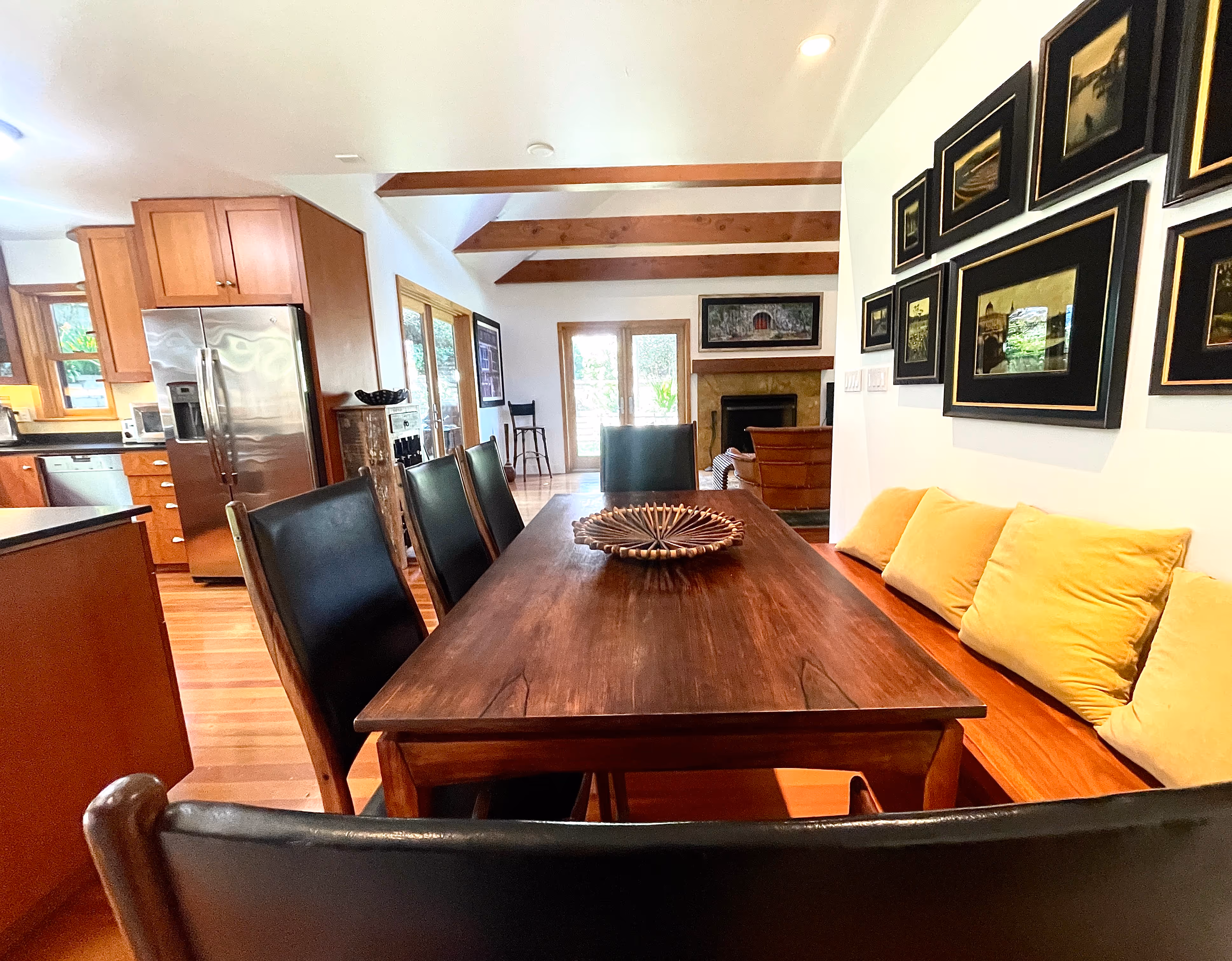 Dining area with a wooden table, black high-back chairs, a built-in wooden bench with yellow cushions, and framed artwork on the wall.