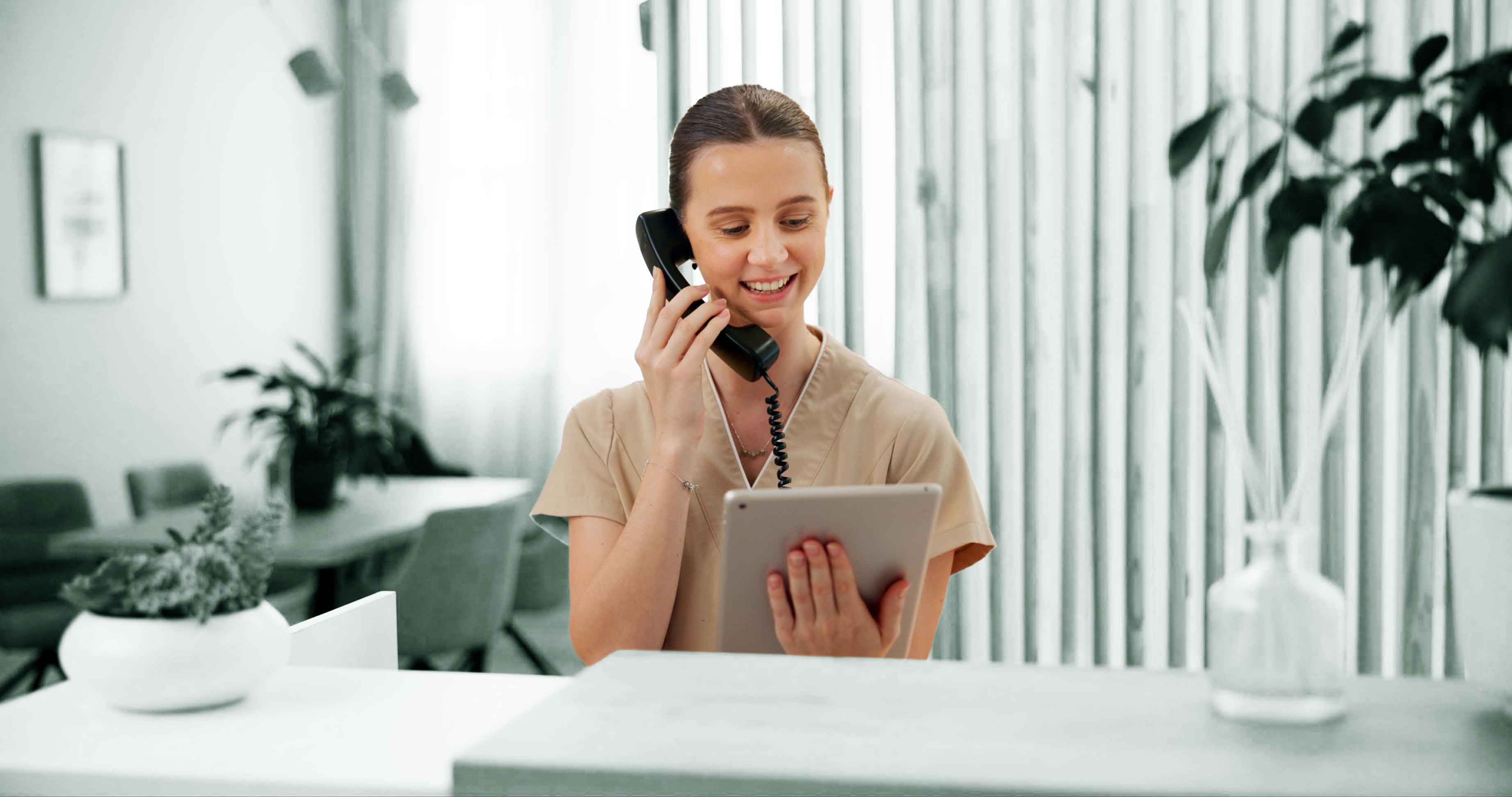 A young dental receptionist is smiling while talking on the phone