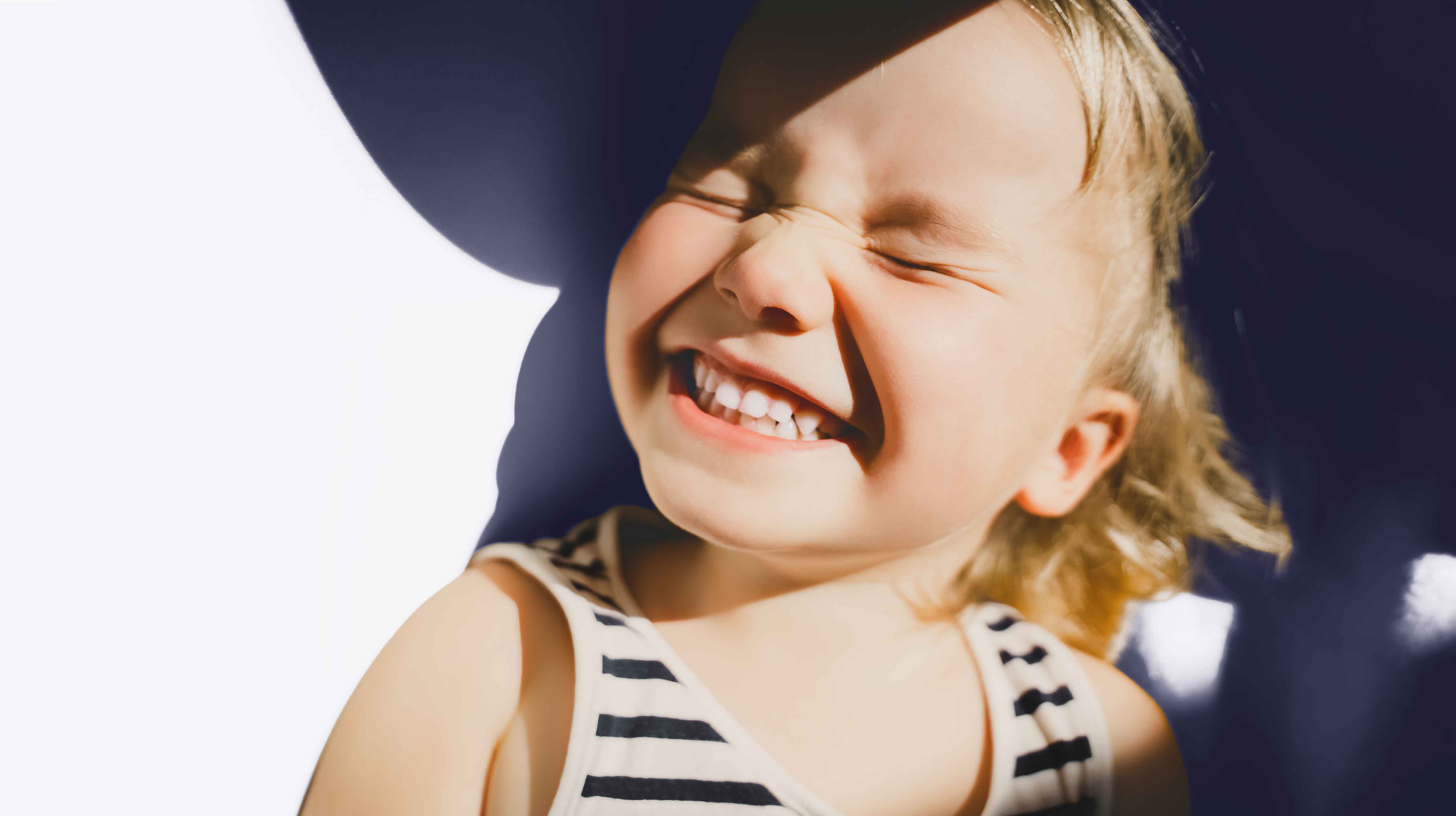 A young girl smiling to show her teeth with her eyes closed