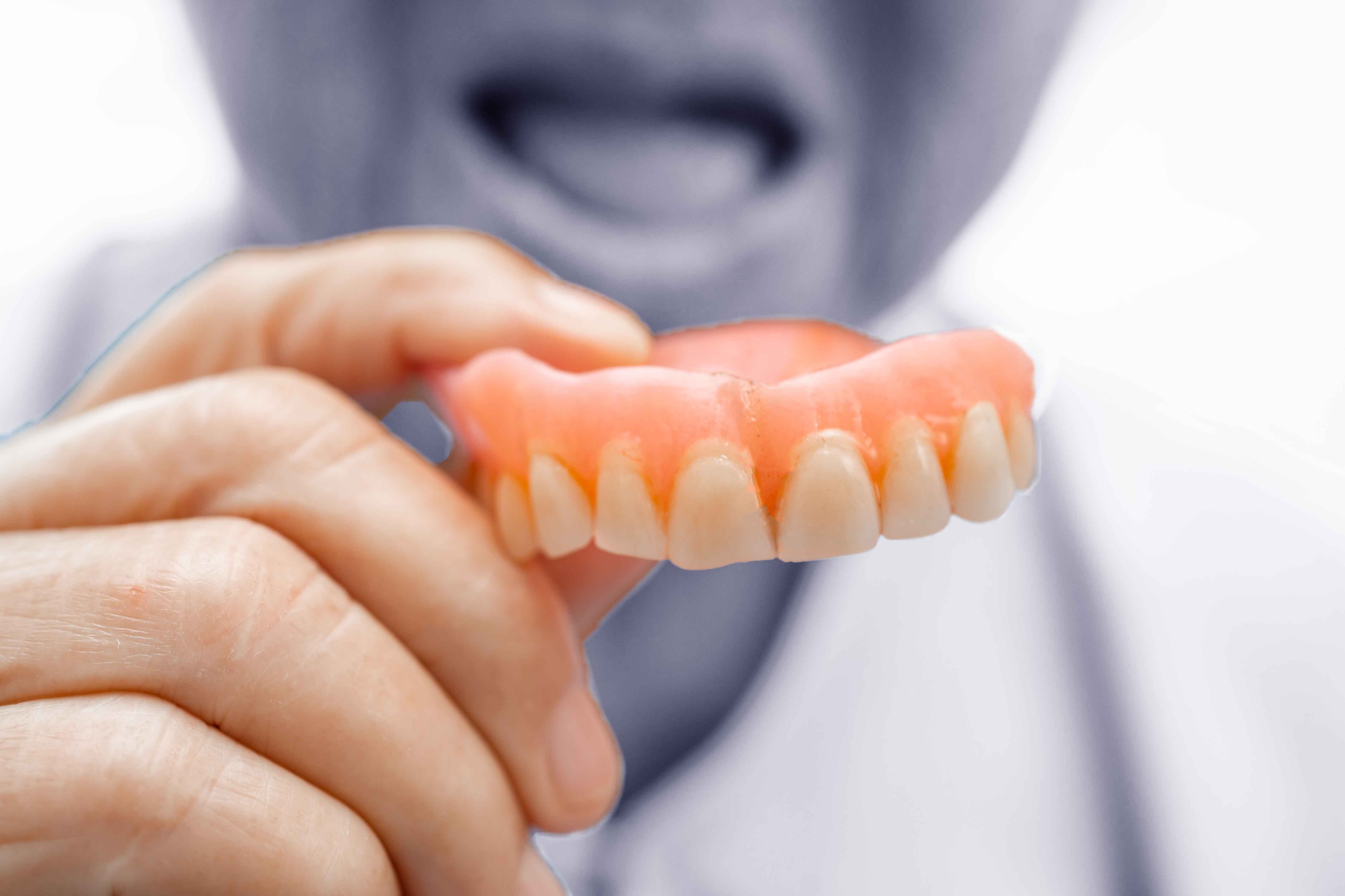 Older man holding his set of false teeth in front of him
