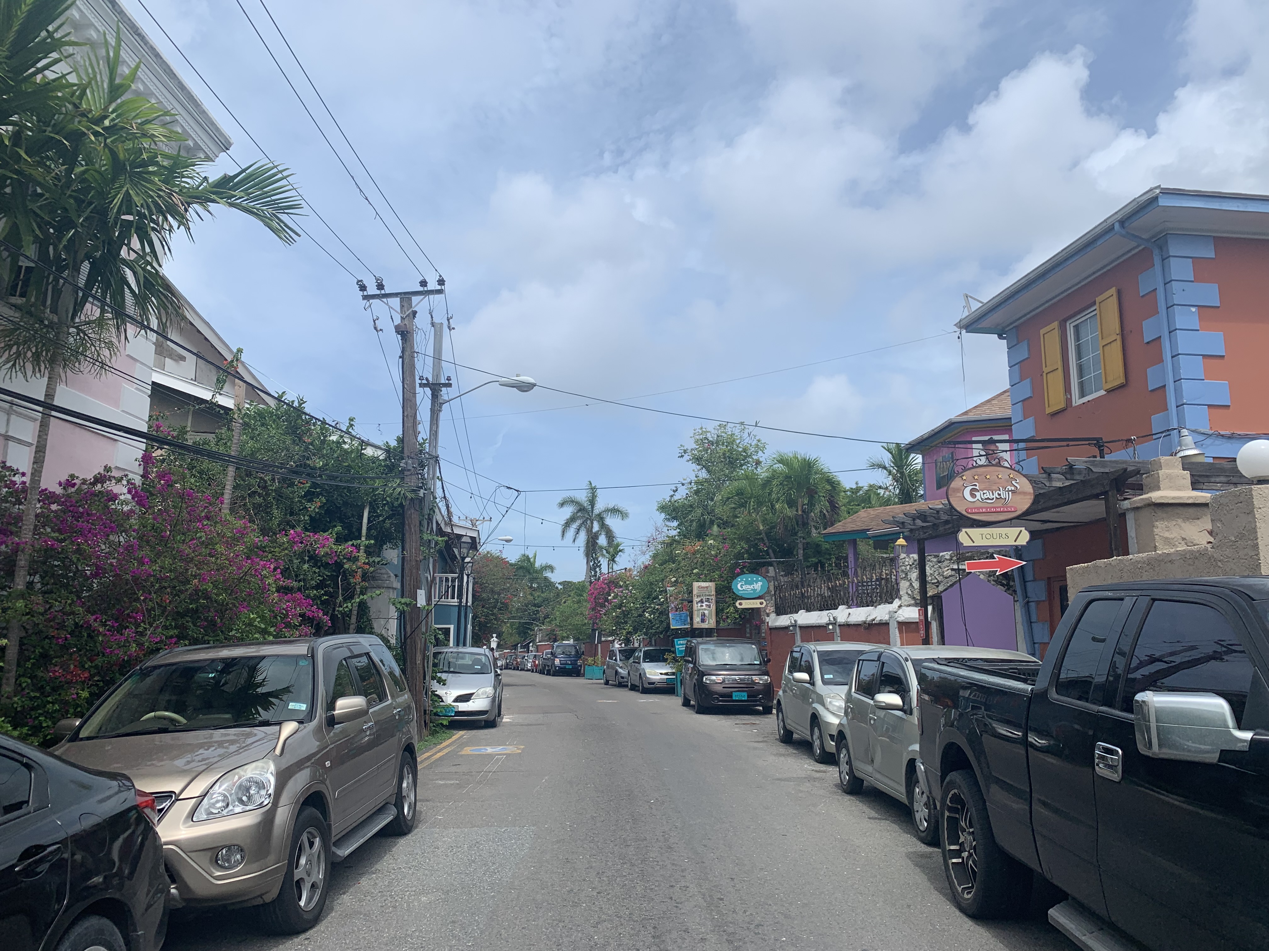 Street with parked cars, palm trees, colorful buildings, and signs pointing to tours on a sunny day.