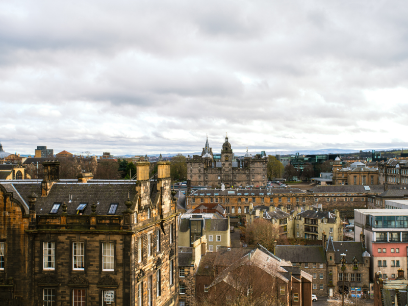 View of historic stone buildings with clock tower under cloudy sky in a cityscape.