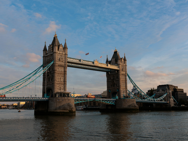 View of Tower Bridge in London spanning the River Thames under a partly cloudy sky.