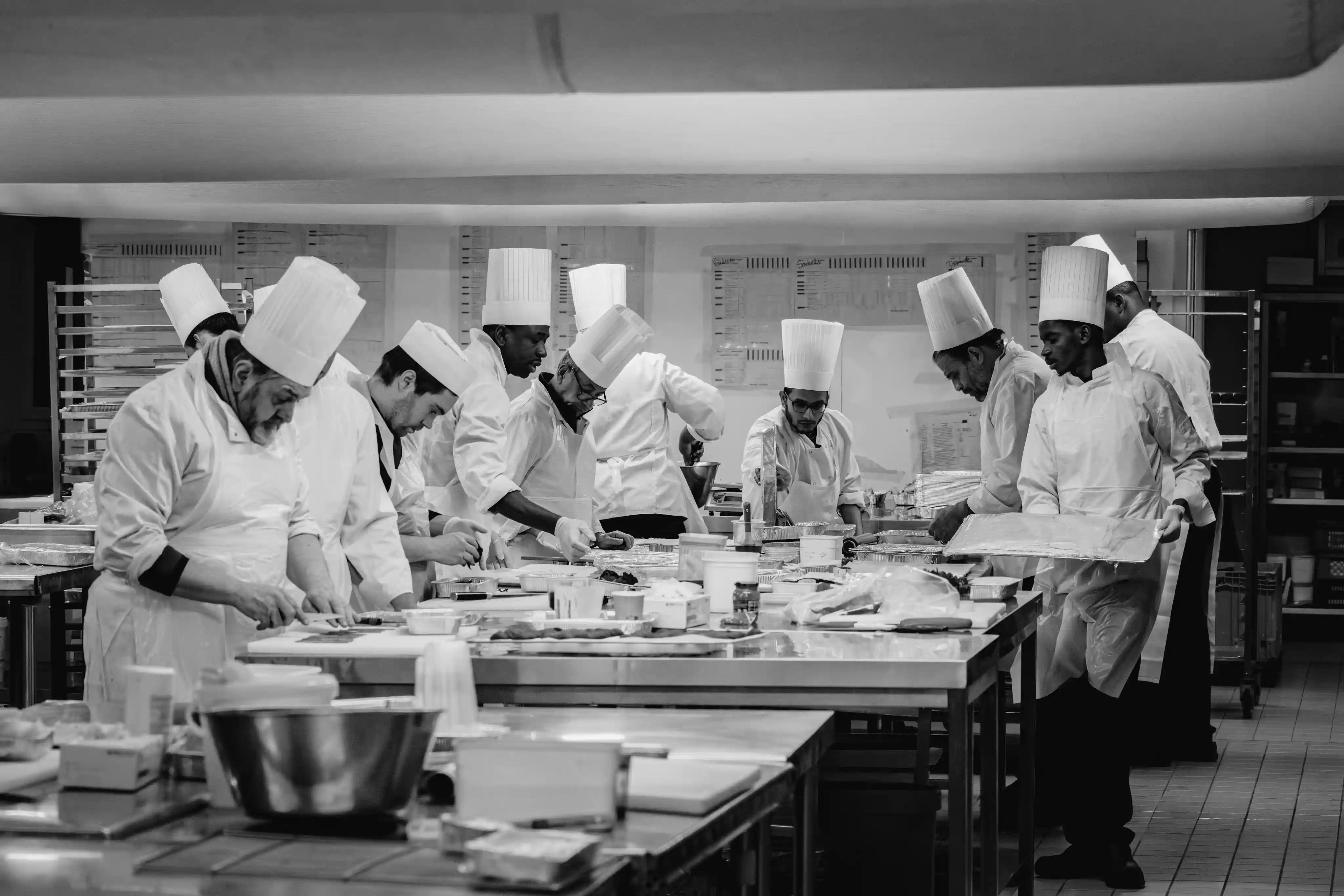 Une équipe de chefs en toque blanche prépare des plats dans une cuisine professionnelle.