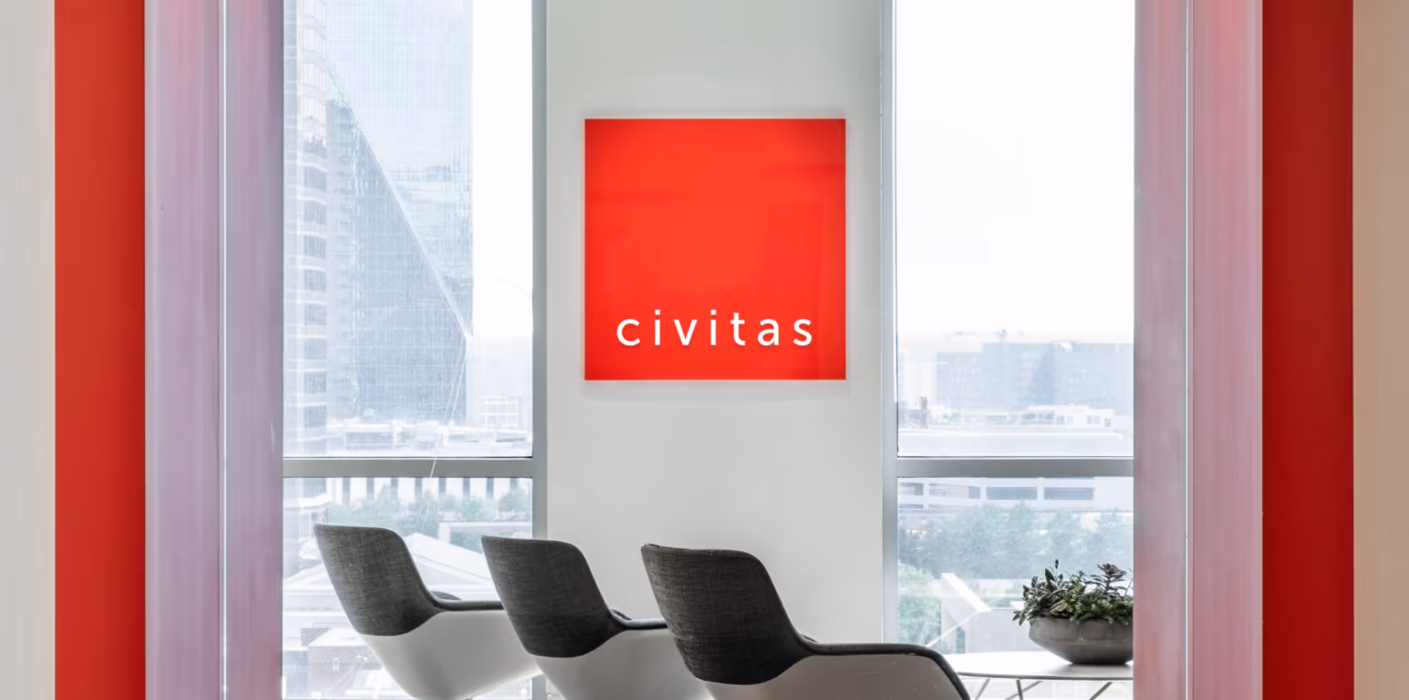 Office interior with three chairs facing large windows and a red illuminated Civitas sign on the wall overlooking a city skyline