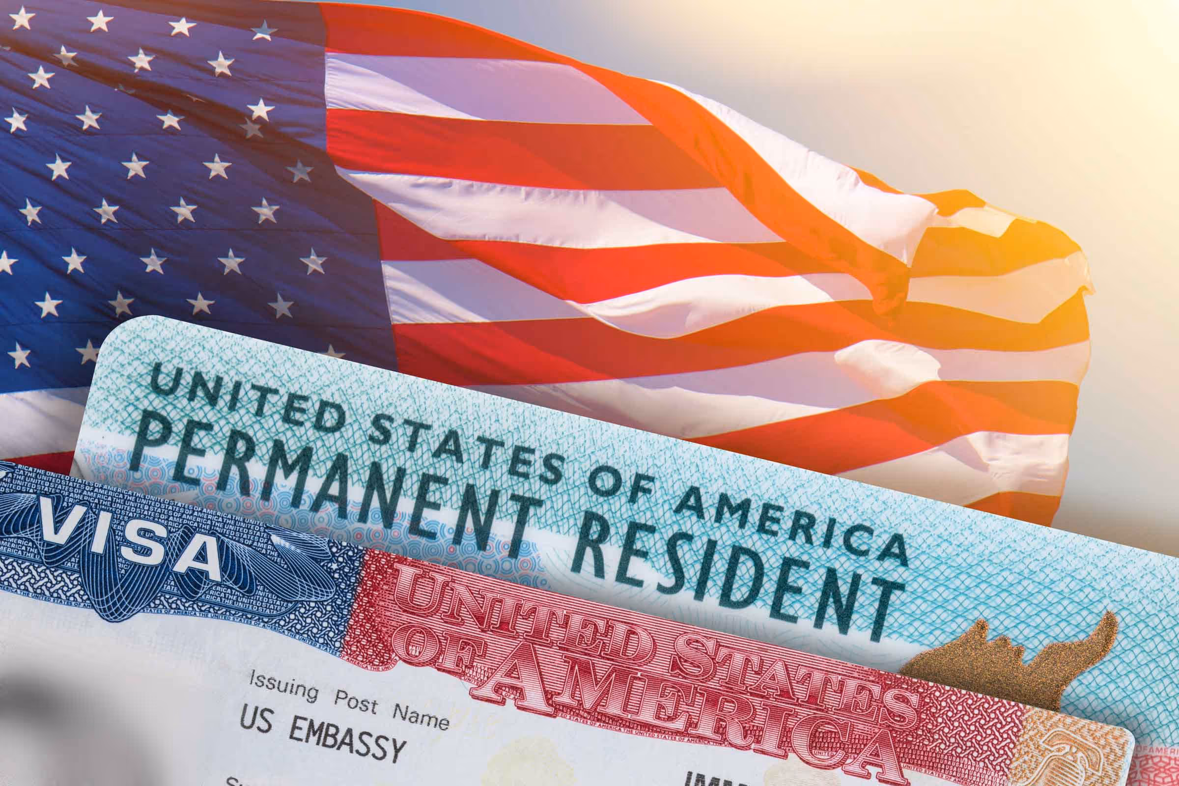Close-up of a United States permanent resident card and visa with a waving American flag in the background.