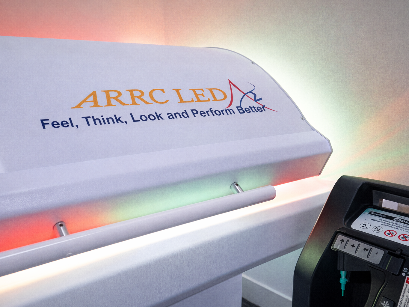 Close-up of a white ARRC LED device with the slogan 'Feel, Think, Look and Perform Better' and colorful LED lights glowing underneath.