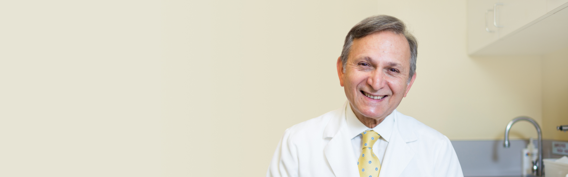 Smiling male doctor in white coat and yellow patterned tie in a medical office.