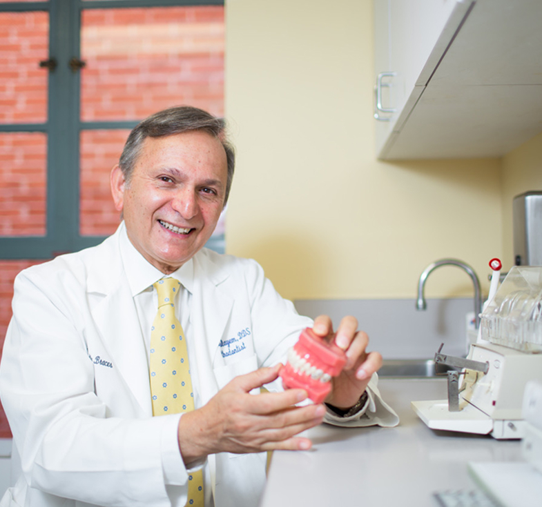Smiling male dentist in a white coat holding a dental model in a clinic.