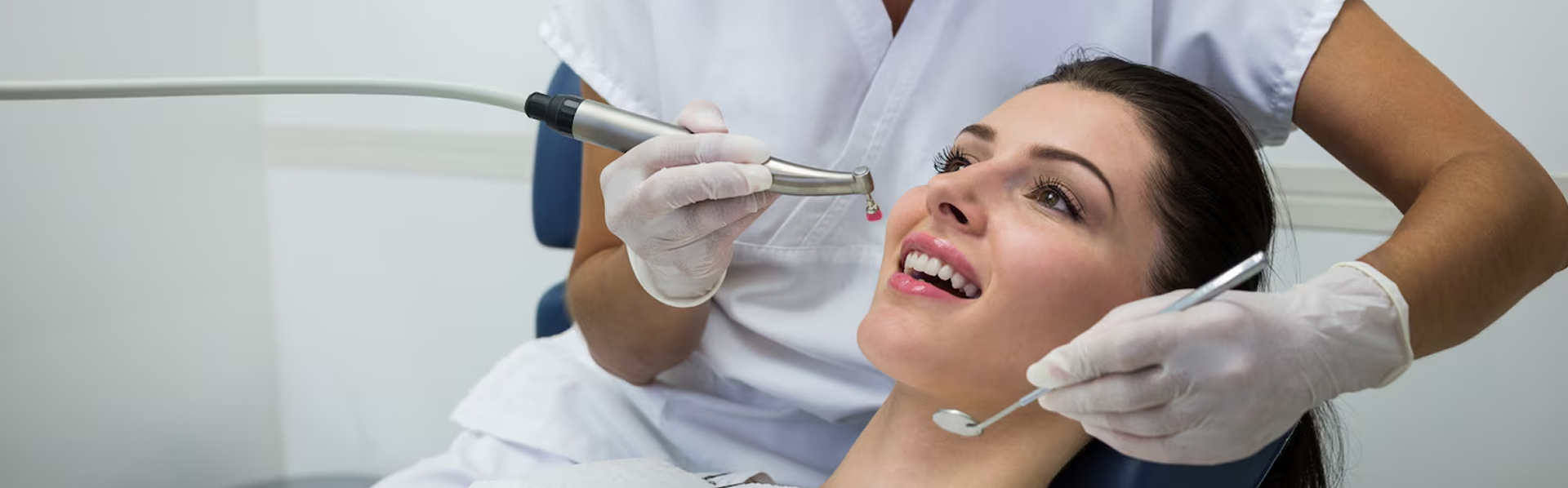 Dentist wearing gloves using dental tools while examining a smiling woman's teeth in a clinic.