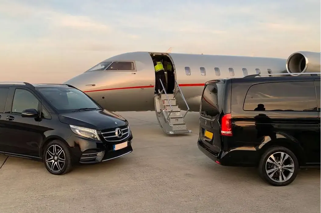 Private jet with stairs down and two black Mercedes vans parked on the tarmac at sunset.