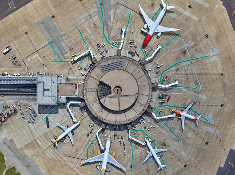 Aerial view of a circular airport terminal with multiple airplanes parked at gates radiating outward.