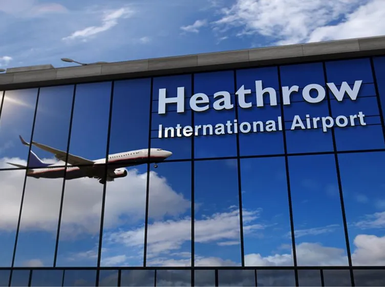 Reflection of an airplane in flight and text reading 'Heathrow International Airport' on glass windows.