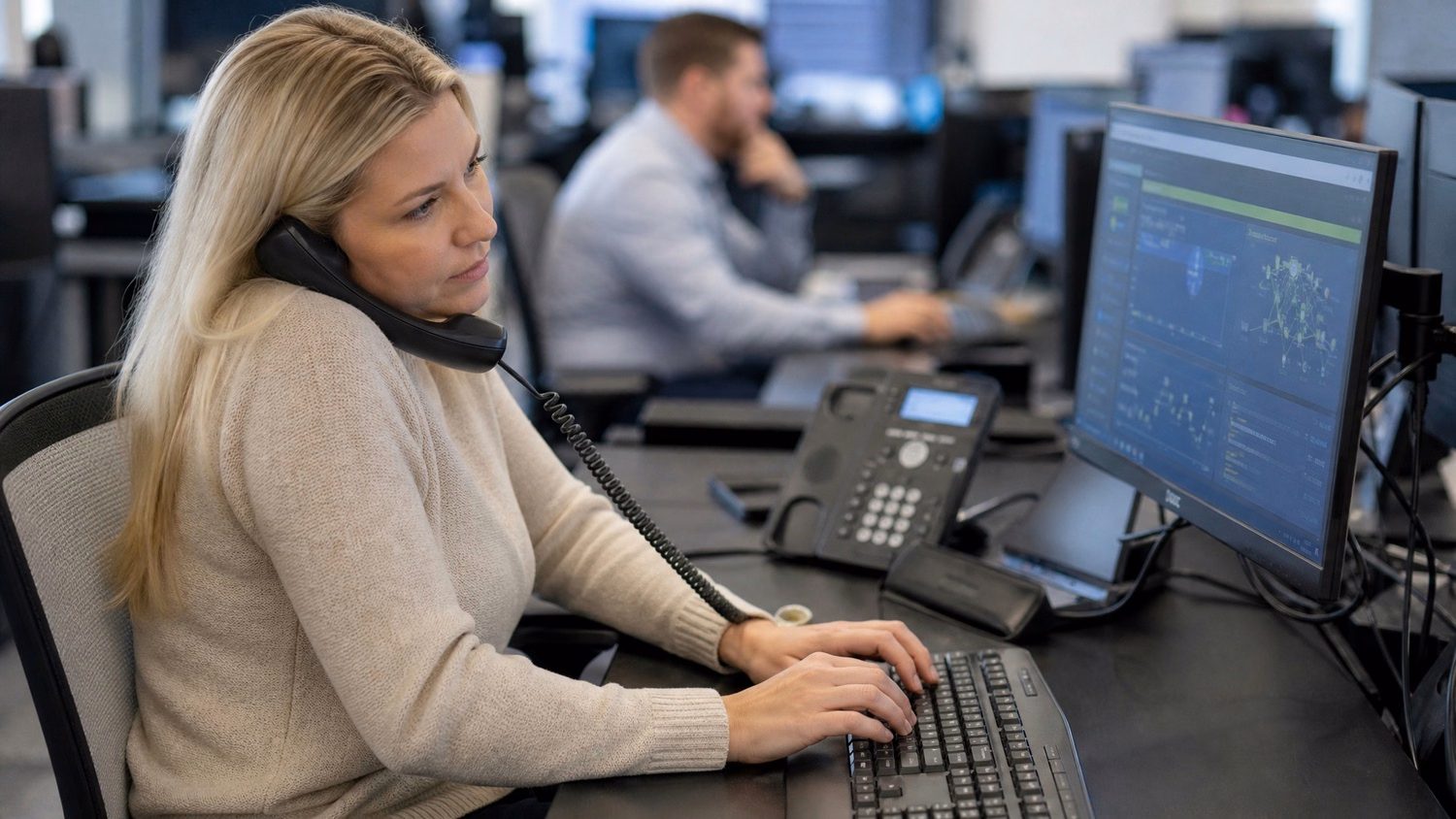 Woman answers desk phone, typing on keyboard, network display 70