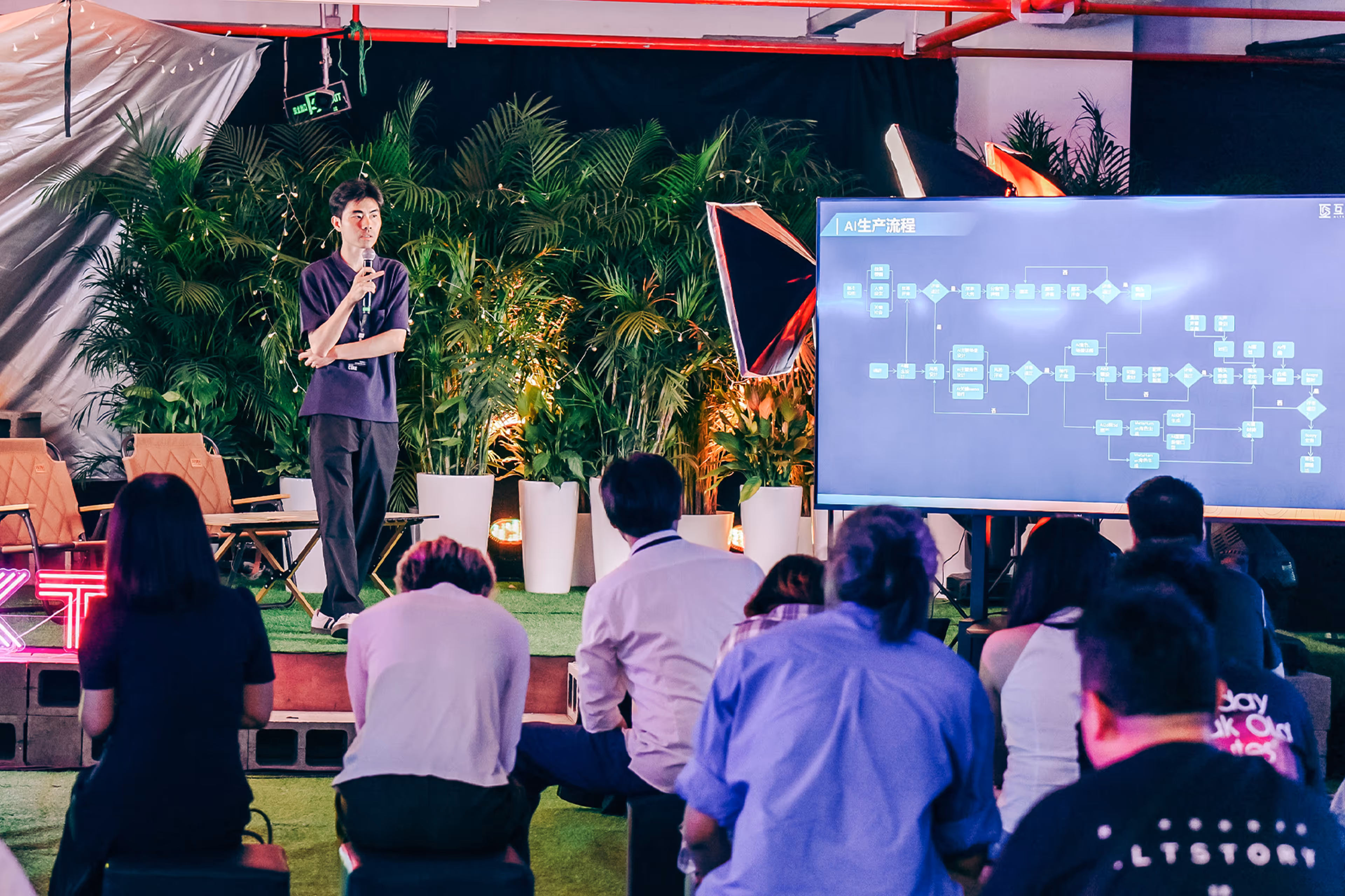 Man speaking with microphone on stage in front of audience, next to a large screen displaying an AI workflow diagram with text in Chinese - at AltNext Edition 1 in 2025