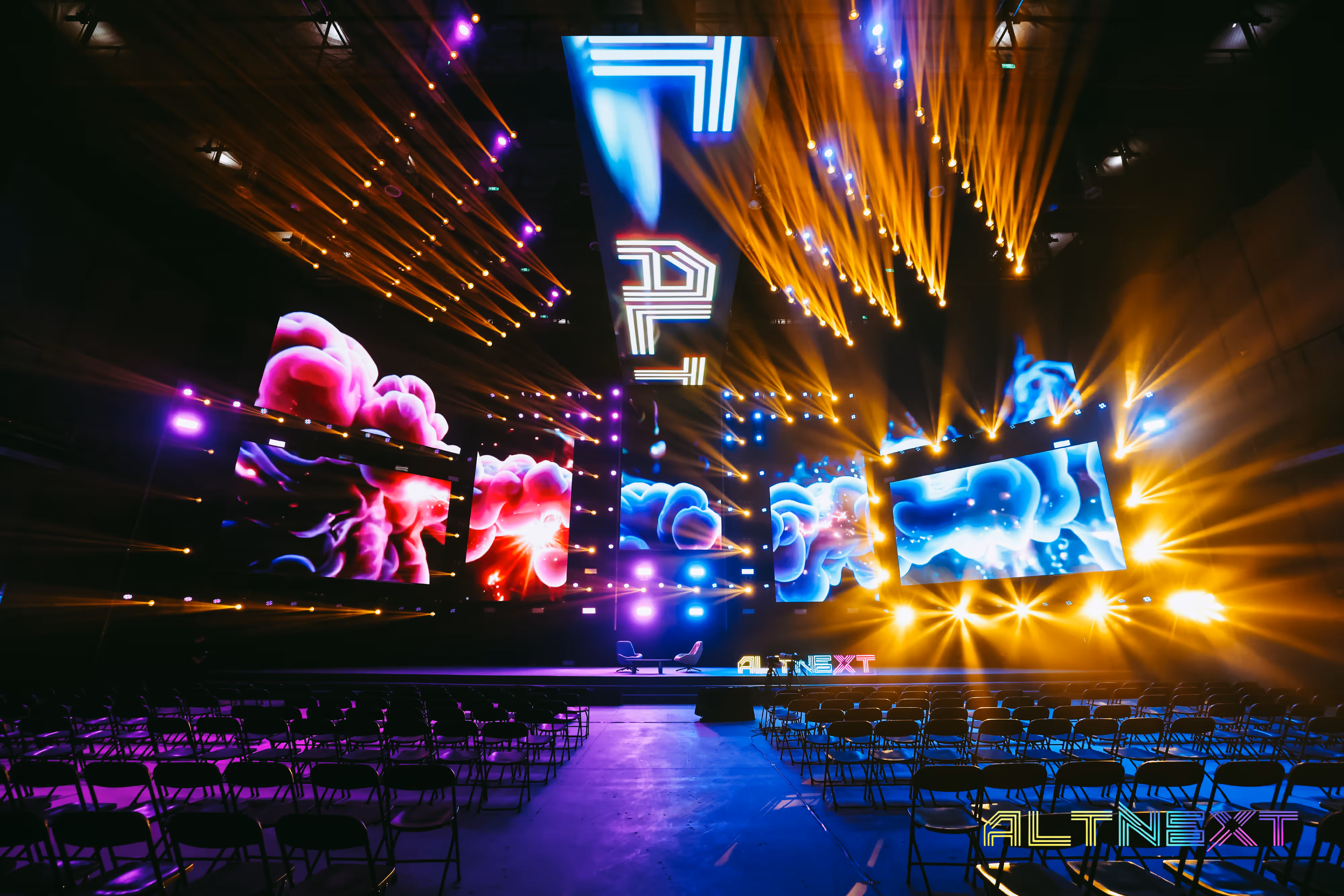 Empty event stage with multiple colorful LED screens and yellow and purple stage lights - at AltNext Edition 1 in 2025.