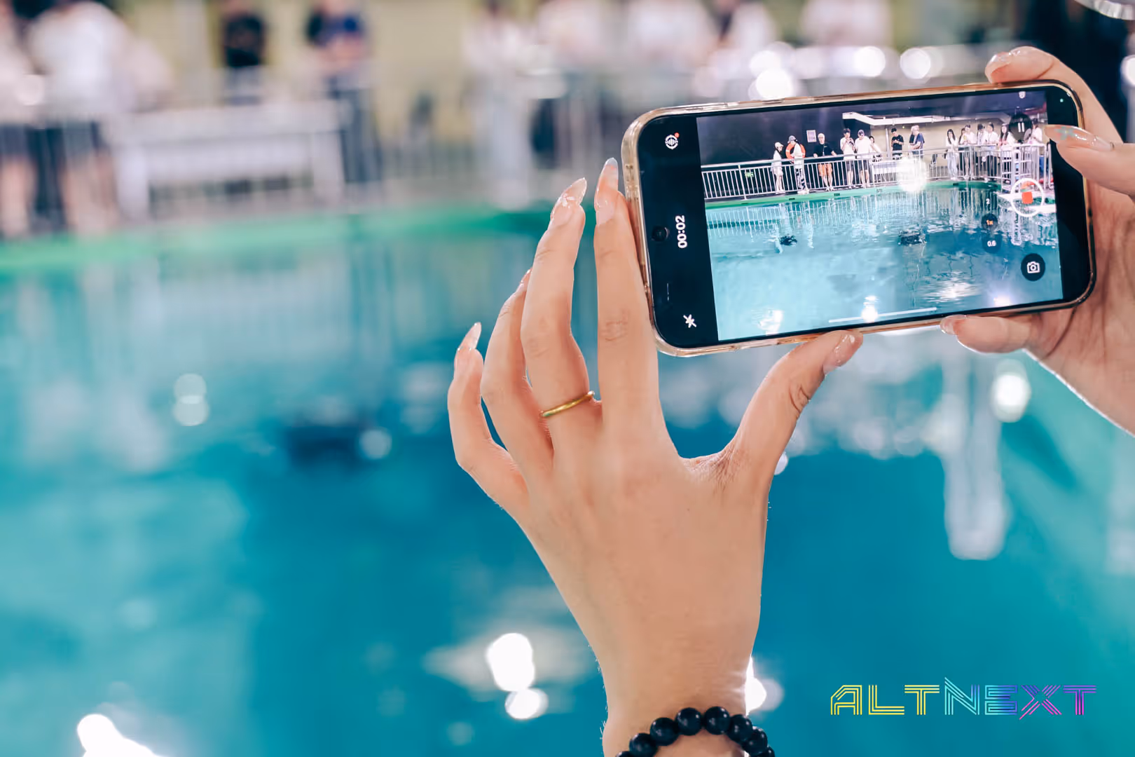 Hand holding smartphone recording a video of people standing around a pool with a railing - at AltNext Season 1 (2025).