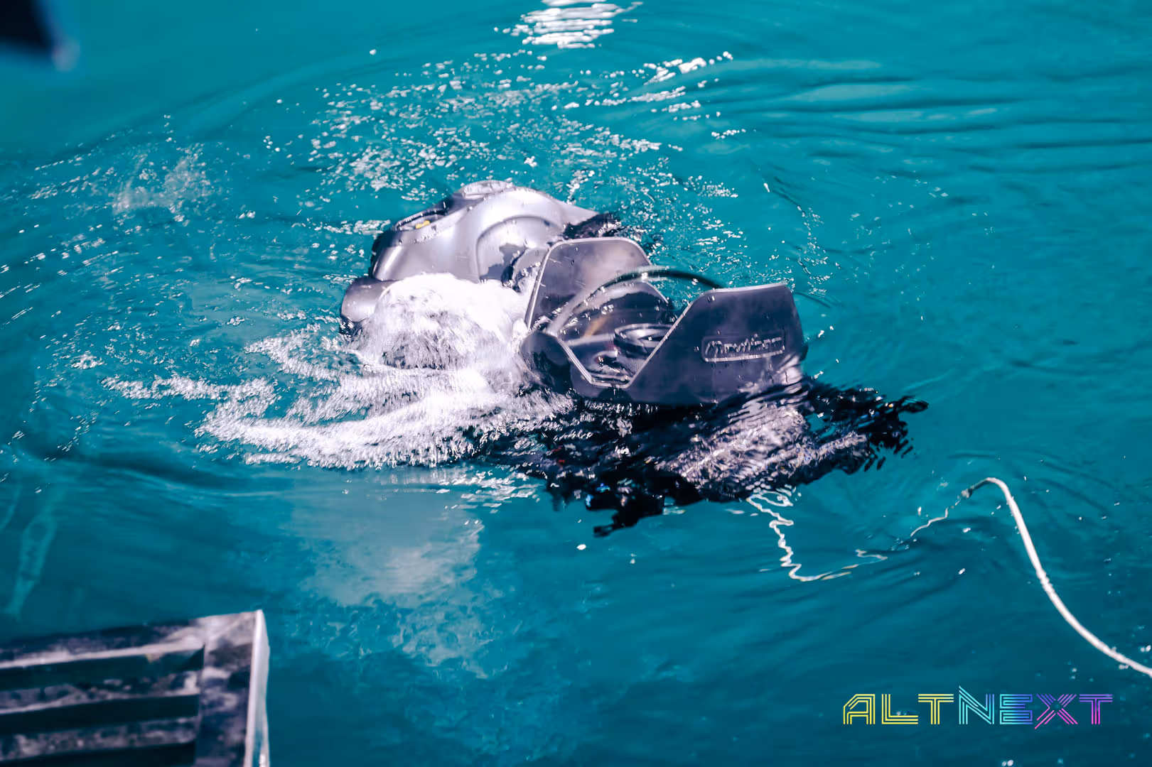 Underwater drone partially submerged in clear blue water creating bubbles as it moves - at AltNext Season 1 (2025).