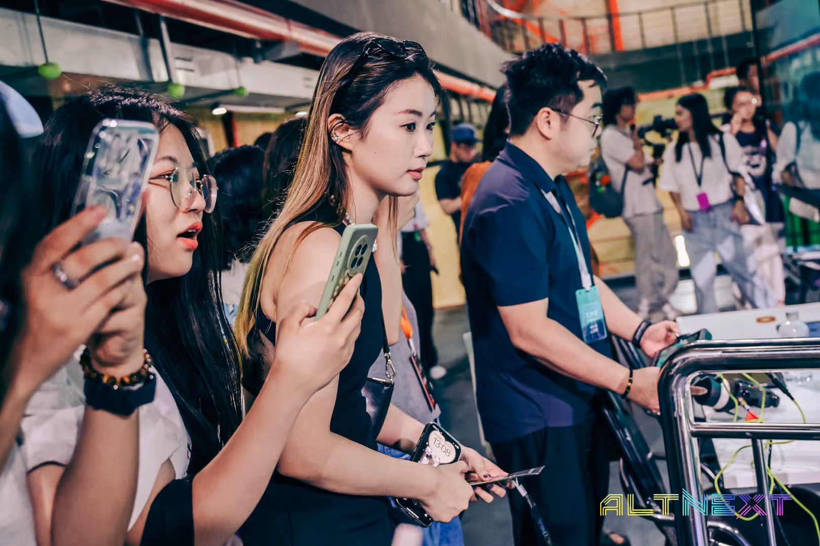 People at a tech event, some holding smartphones and cameras, with 'ALTNEXT' logo in the corner - at AltNext Season 1 (2025).