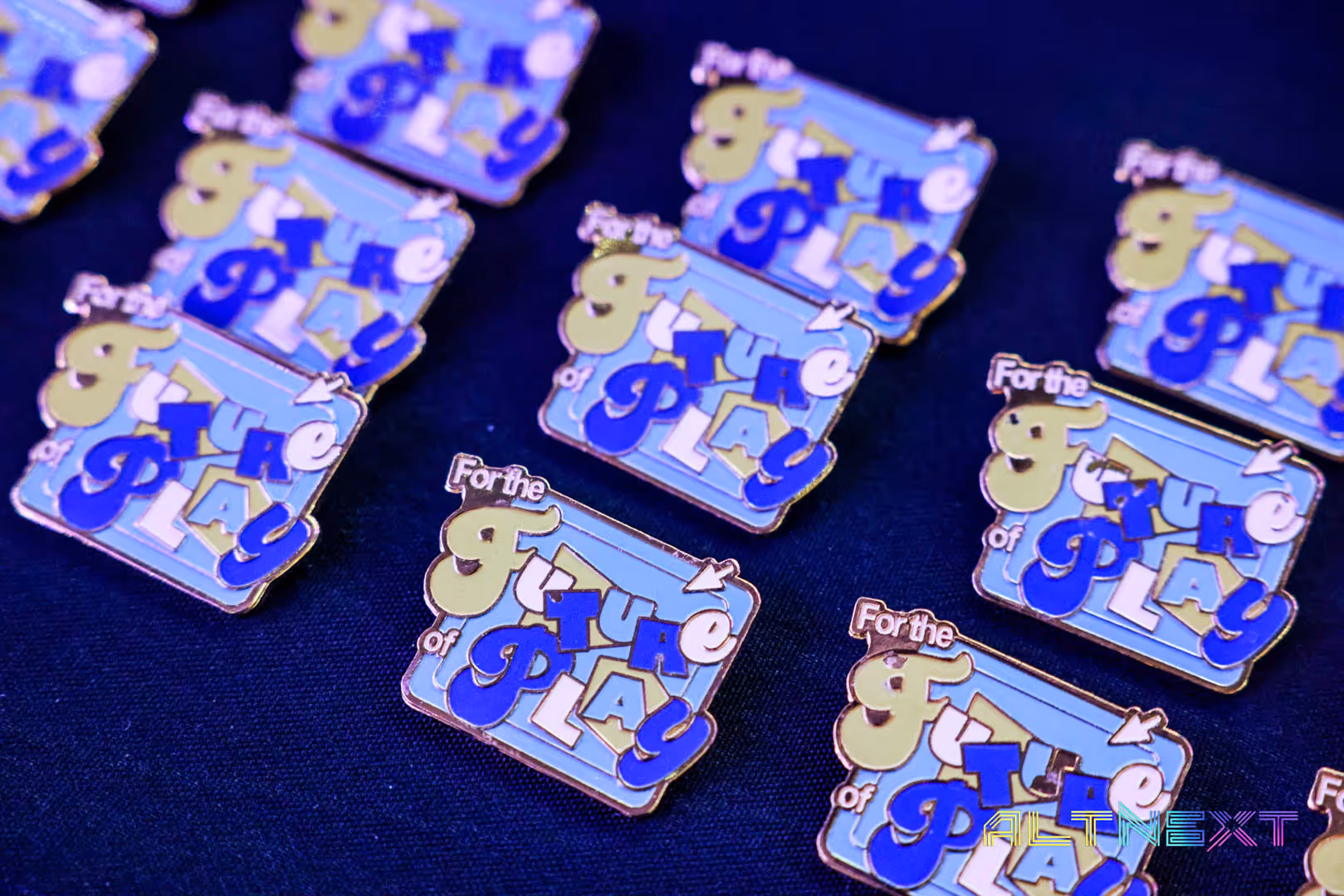 Several enamel pins with the phrase 'For the Future of Play' in playful blue and yellow lettering on a blue background - at AltNext Season 1 (2025).