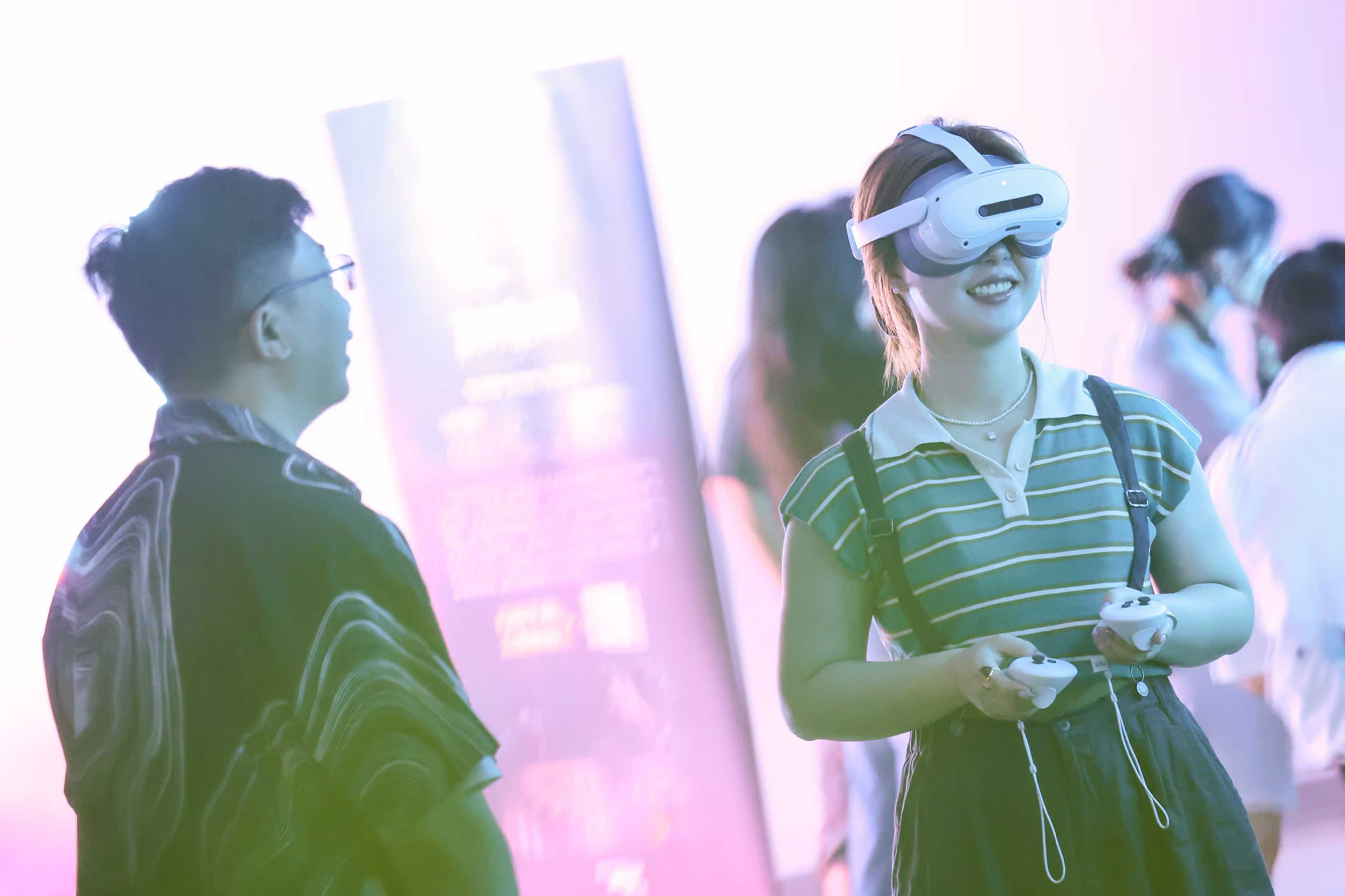 Young woman wearing a virtual reality headset and holding controllers smiles while interacting with a man in a vibrant, softly lit environment - at AltNext Edition 1 in 2025.