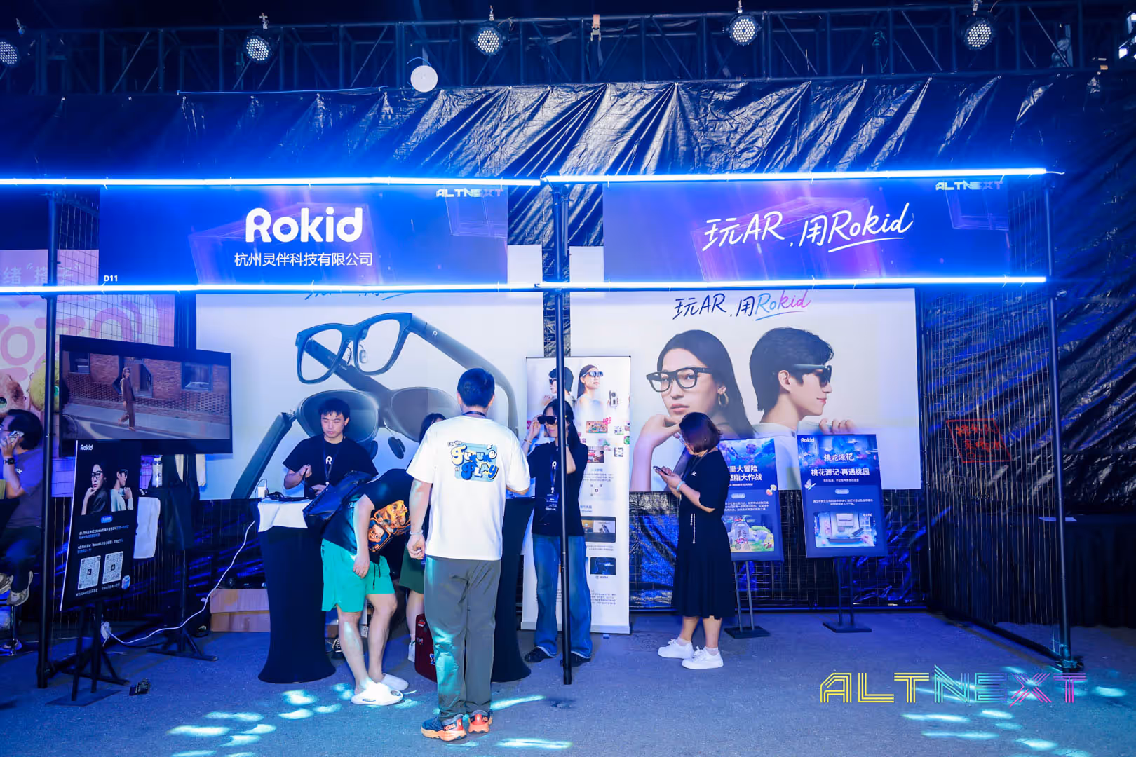 Rokid technology booth at AltNext featuring AR smart glasses with people interacting and promotional banners in blue lighting.