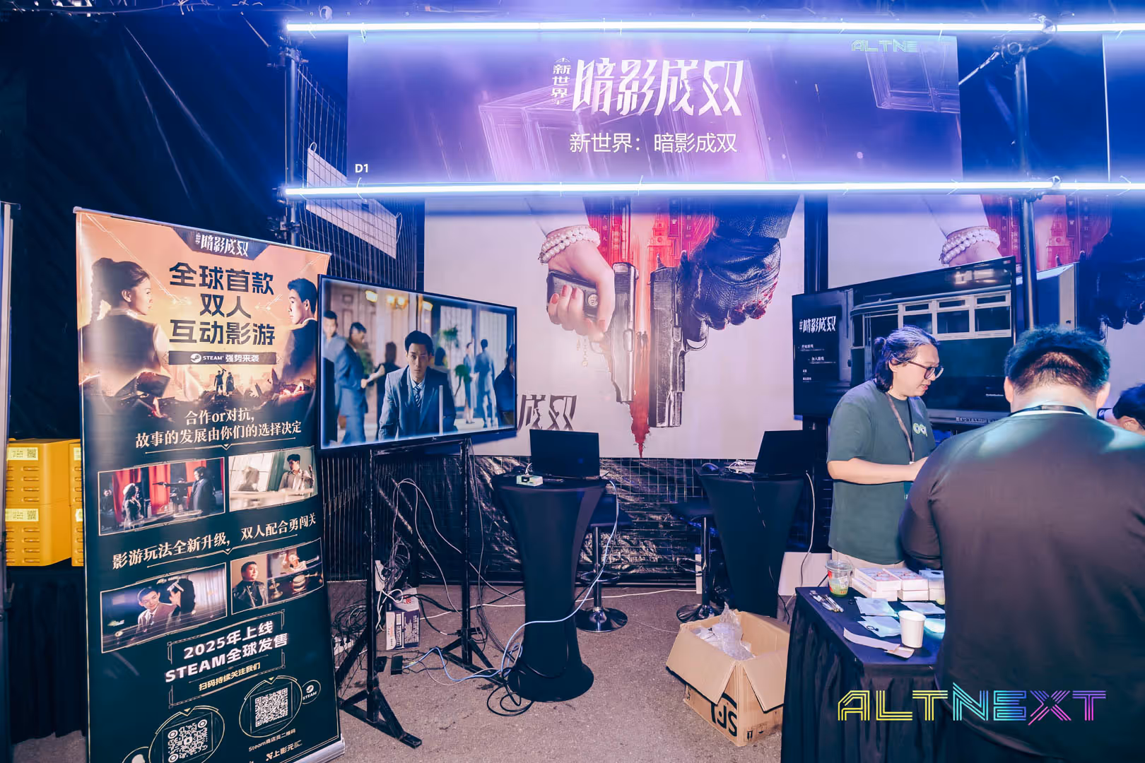 Exhibition booth with large posters, two screens showing scenes from a film, and people interacting at a table during a gaming event - at AltNext Edition 1 in 2025.