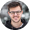 Homme portant des lunettes souriant devant un fond neutre flou.