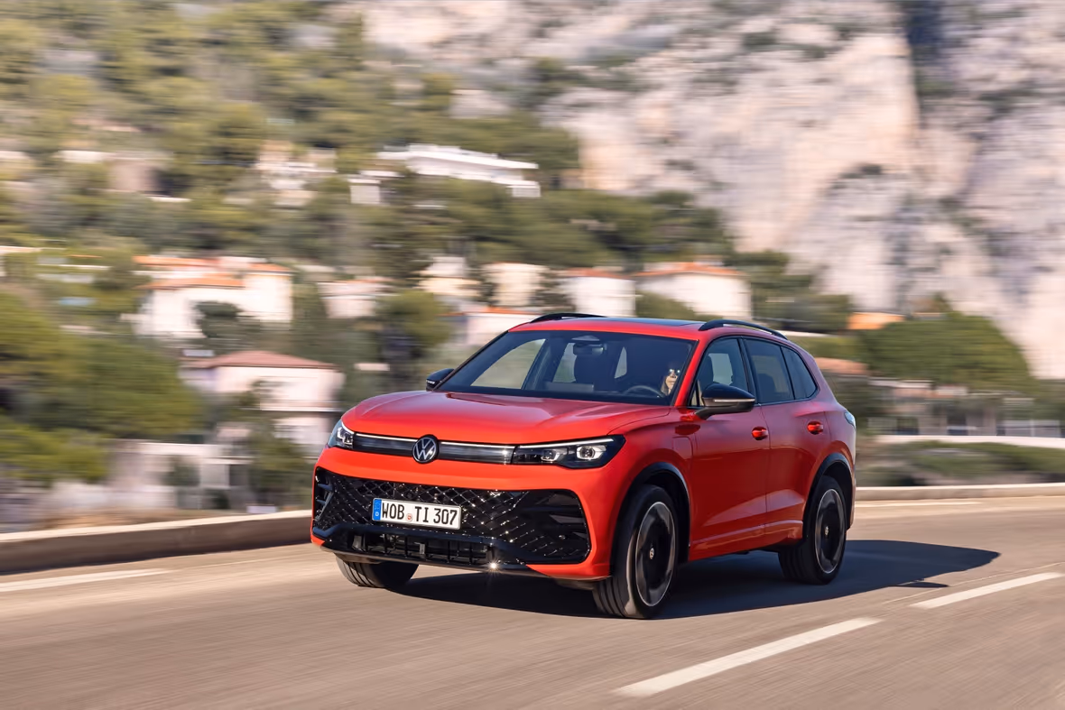 Roter Volkswagen SUV fährt auf einer Straße mit unscharfem Hintergrund aus Bäumen und Gebäuden.