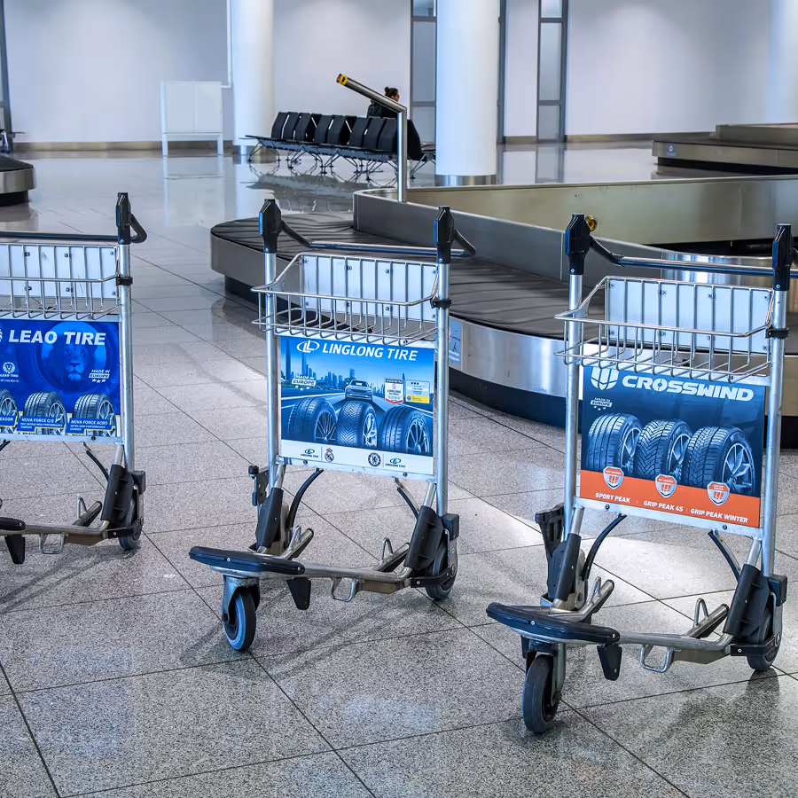 Drei Gepäckwagen mit Werbung für Autoreifenmarken Leao Tire, Linglong Tire und Crosswind in einem Flughafen-Gepäckbereich.