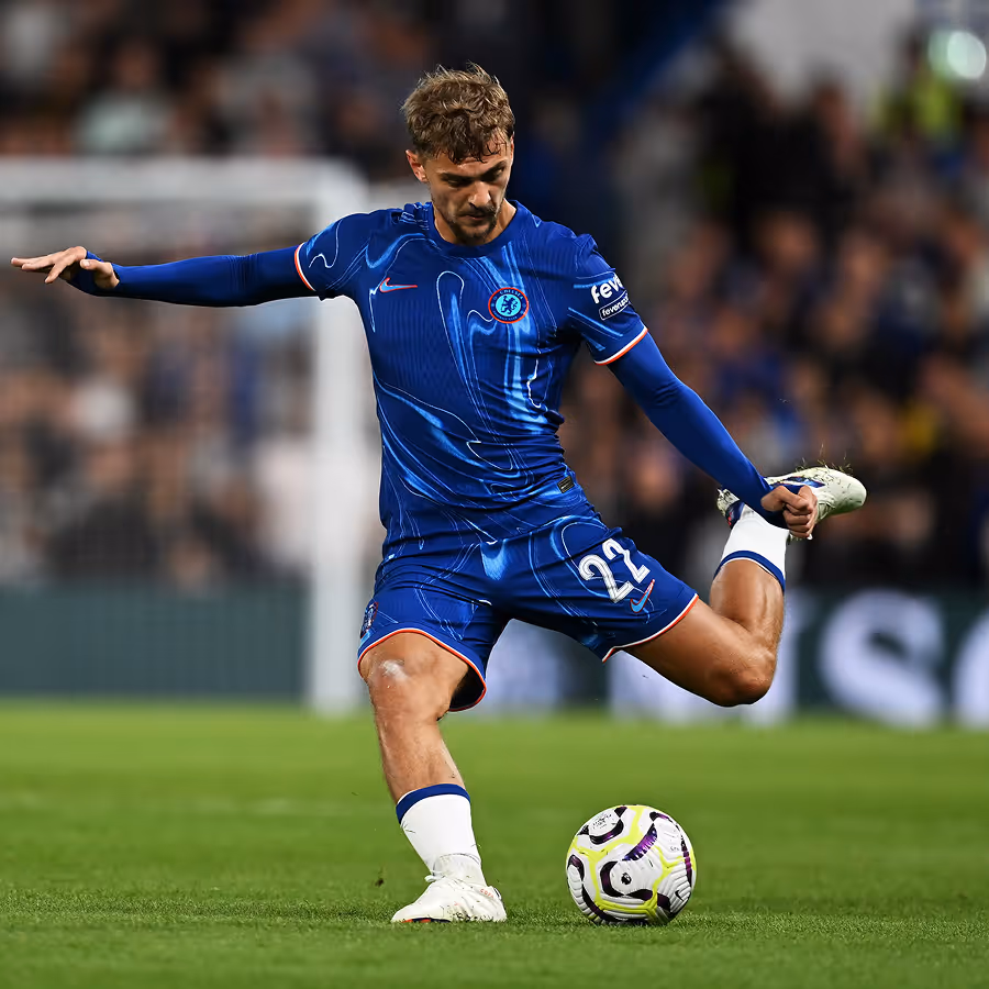 Fußballspieler in blauem Chelsea-Trikot schießt den Ball auf dem Spielfeld.