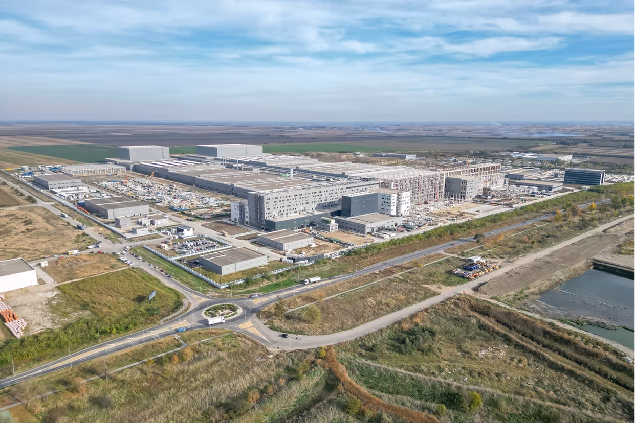 Luftaufnahme eines großen Industriekomplexes mit mehreren Gebäuden und Parkplätzen in einer ländlichen Umgebung.