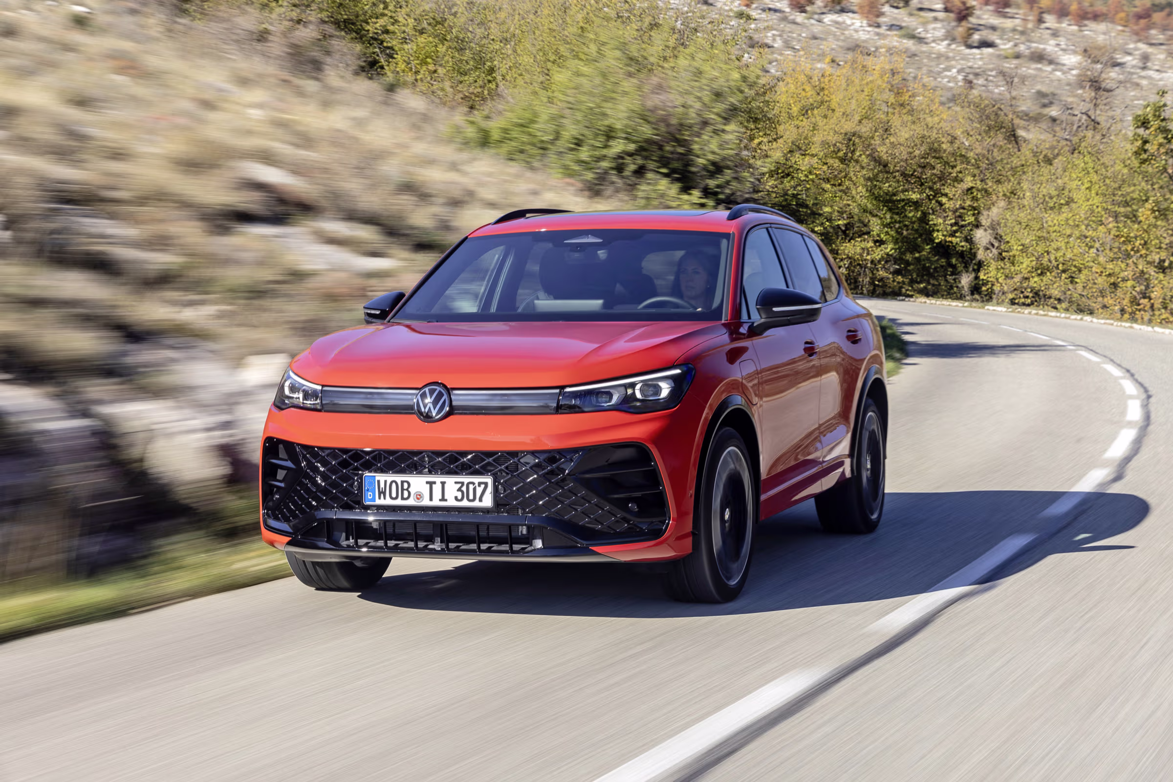 Roter Volkswagen SUV fährt auf einer kurvigen Landstraße bei sonnigem Herbstwetter.