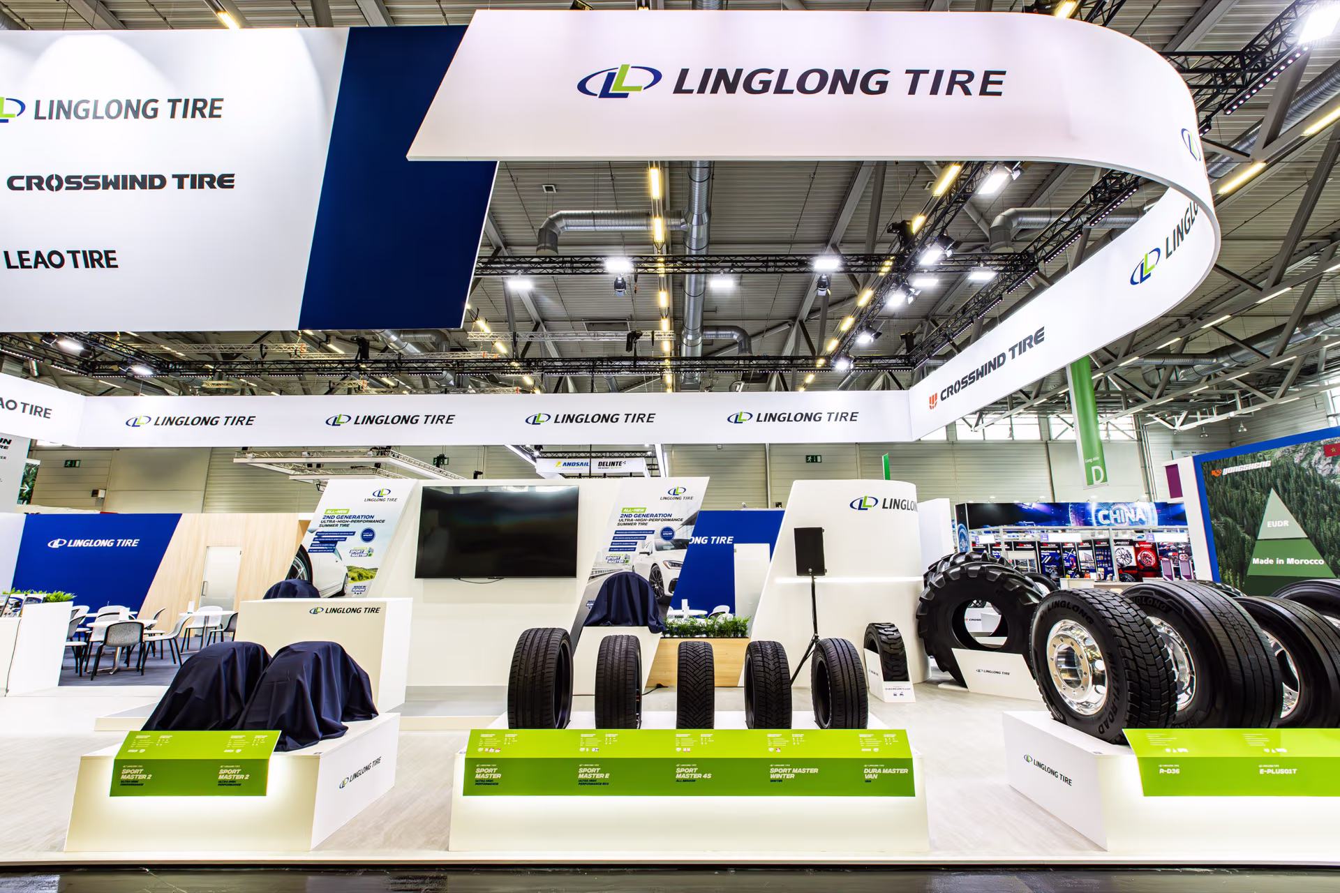 Messestand von Linglong Tire mit verschiedenen Autoreifen auf weißen Podesten und einem großen weißen Banner mit dem Linglong Tire Logo und weiteren Markennamen wie Crosswind Tire und Leao Tire.